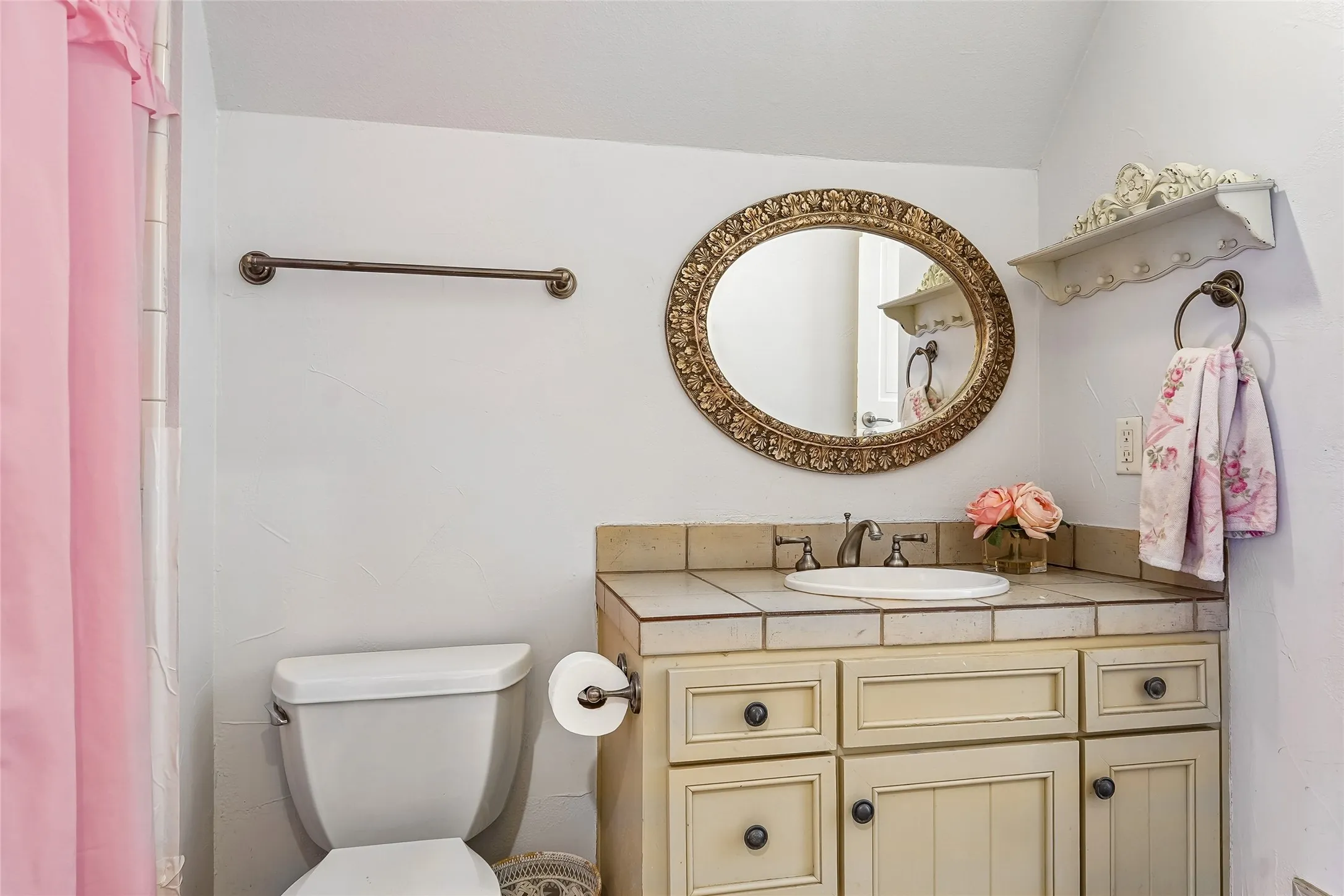 Bathroom vanity featuring tile countertop, inset basin, oval decorative mirror, and wall-mounted shelving