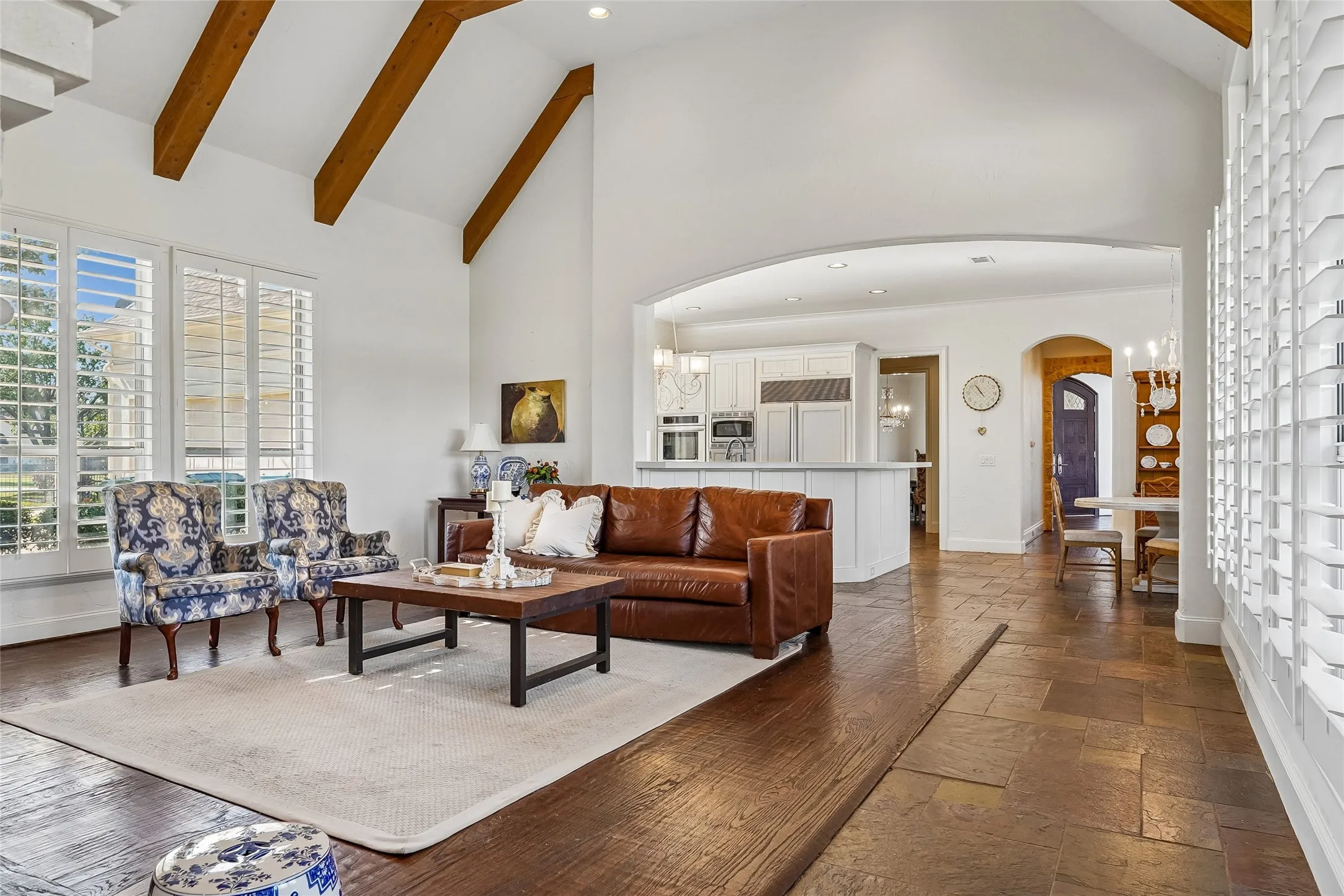 Vaulted ceiling with exposed wood beams, stone tile flooring, and plantation shutters
