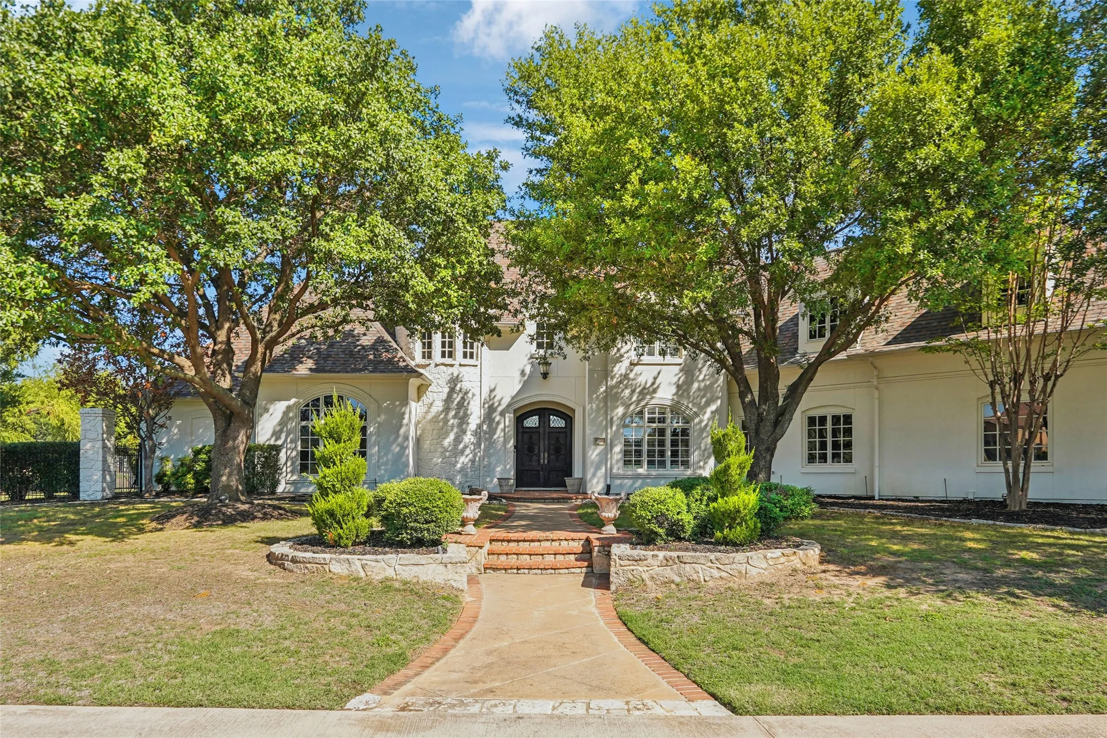 Light-colored masonry exterior featuring a multi-gabled roofline, arched window detailing, stone-accented front entryway, and mature landscaping