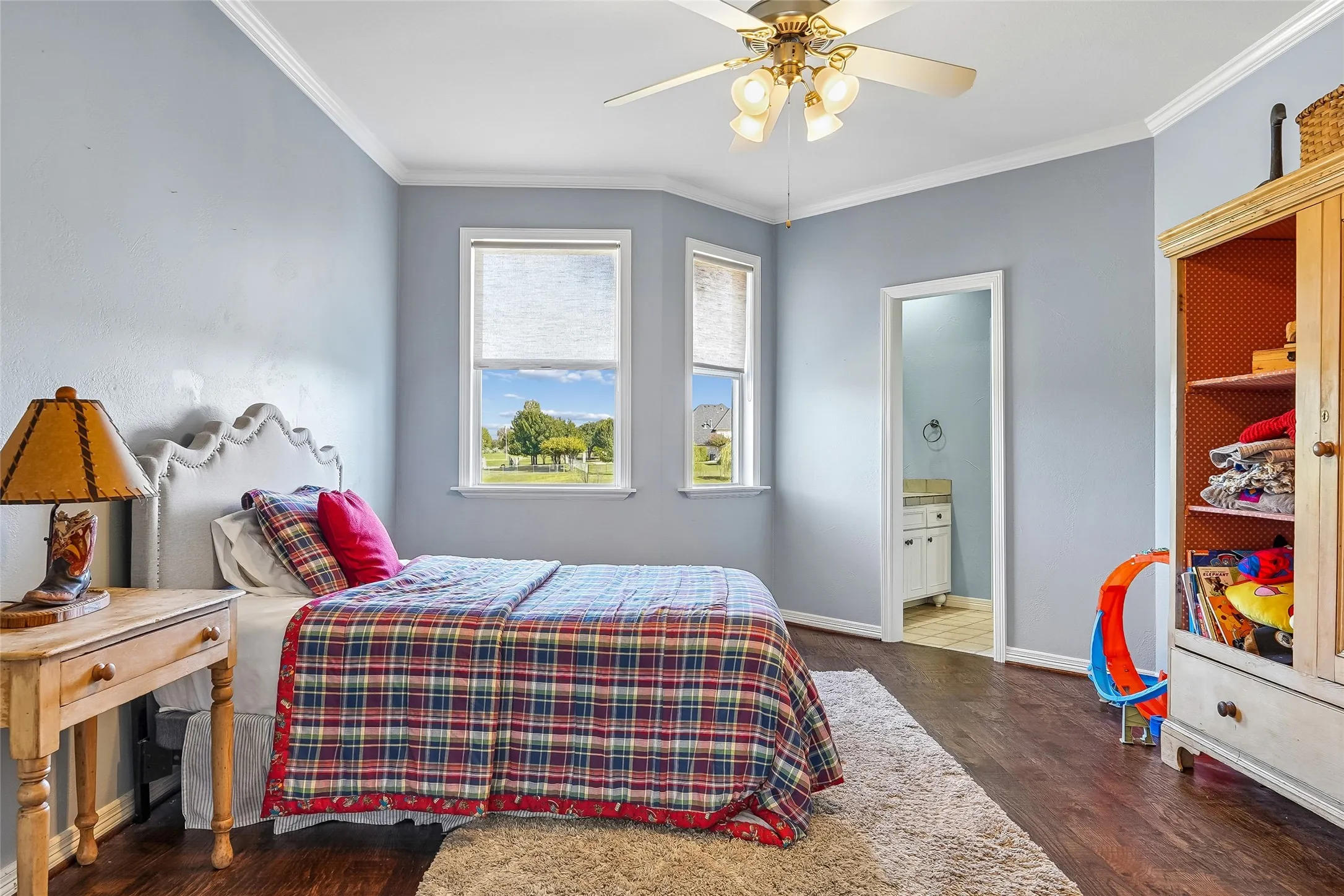 Multi-pane bay windows, dark wood-finish flooring, ceiling fan with integrated lighting, and crown molding