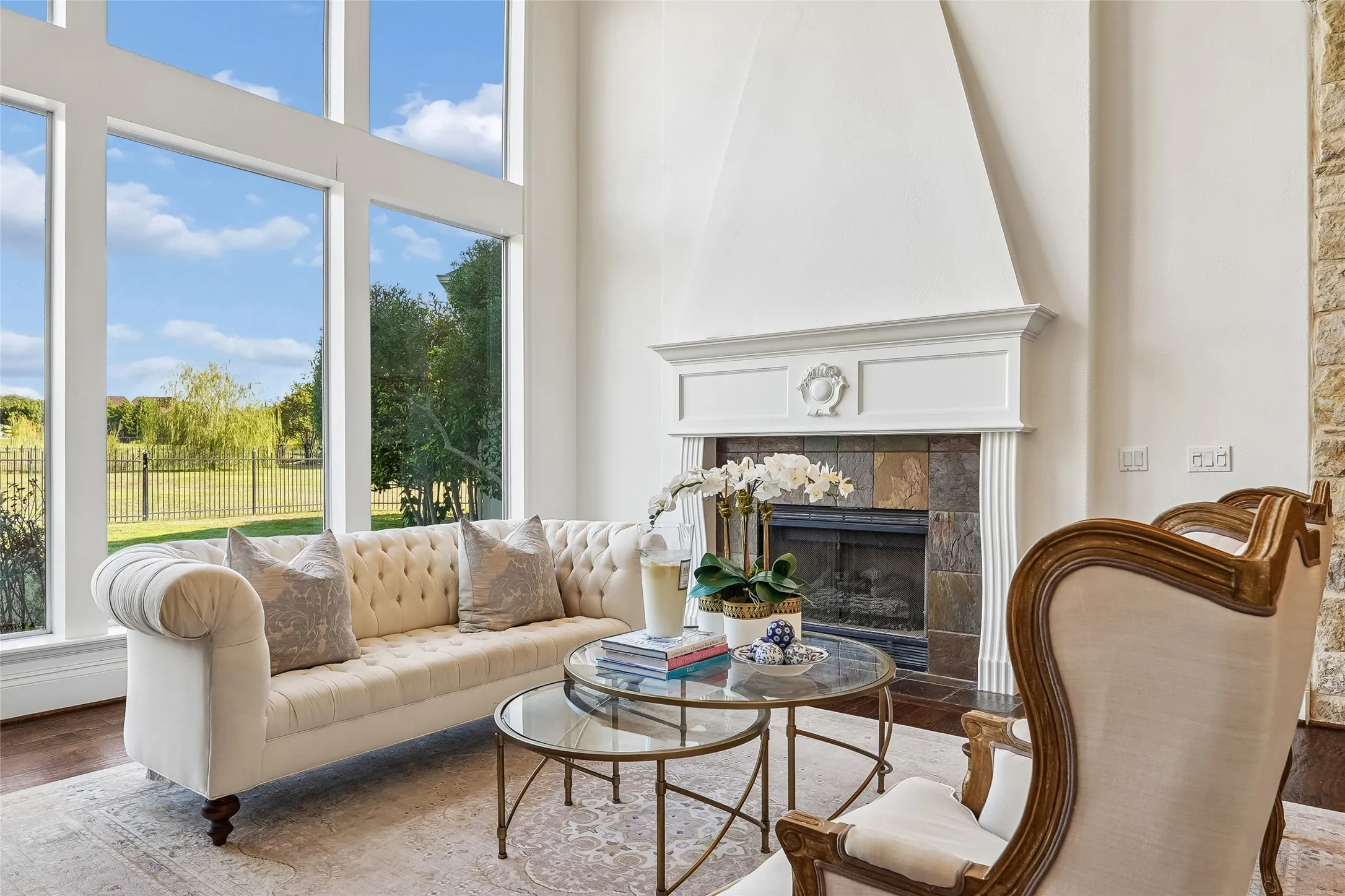 Double-height windows, floor-to-ceiling stone-accented fireplace surround, white millwork mantelpiece, and dark wood-finish flooring