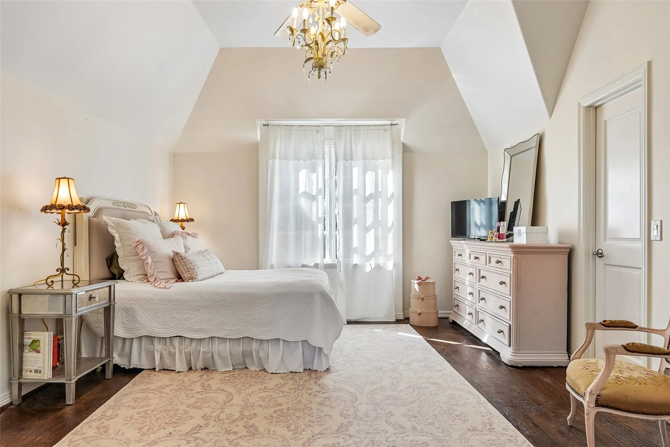 Vaulted ceiling featuring an ornate central chandelier, wood-finish flooring, and multi-pane window