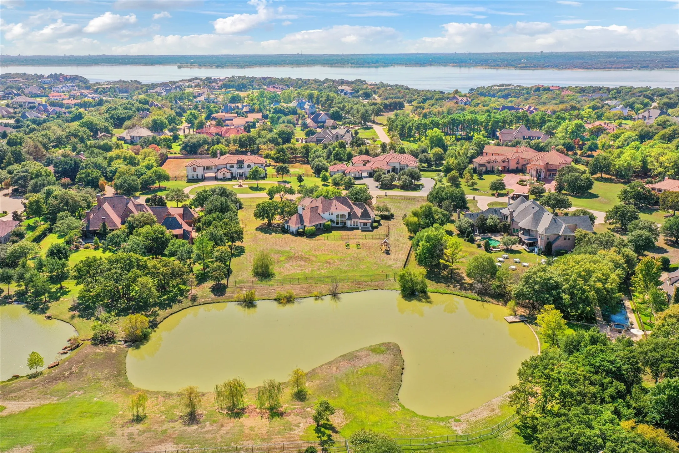 Aerial perspective of a sprawling residential lot featuring a private pond, open acreage, mature trees, and proximity to the shoreline
