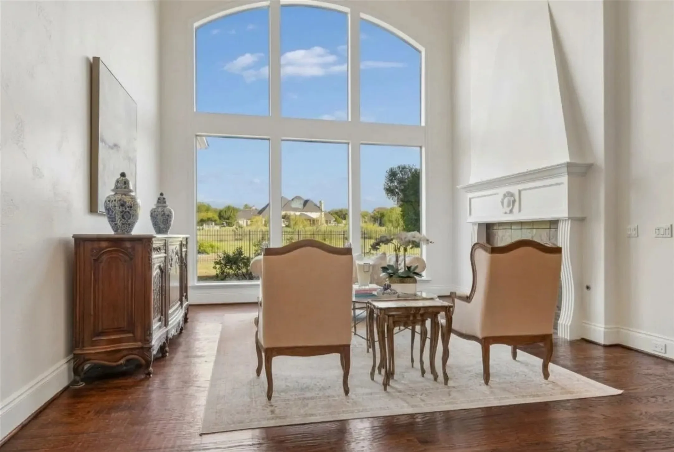 Double-height living area featuring an expansive arched window, wood-finish flooring, and a fireplace with a decorative mantel