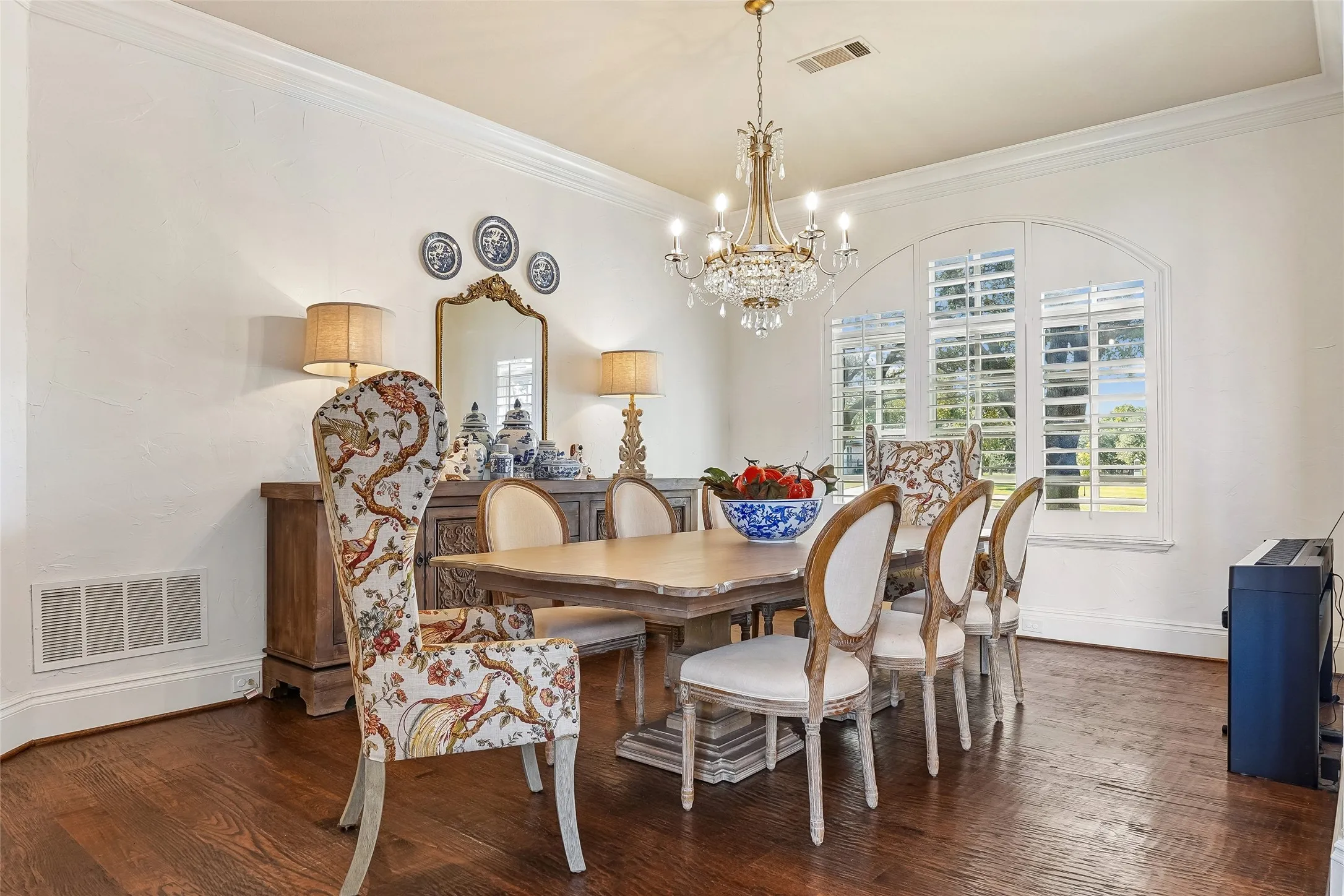 Dining area featuring wood-finish flooring, an arched window with plantation shutters, crown molding, and a multi-tiered crystal chandelier