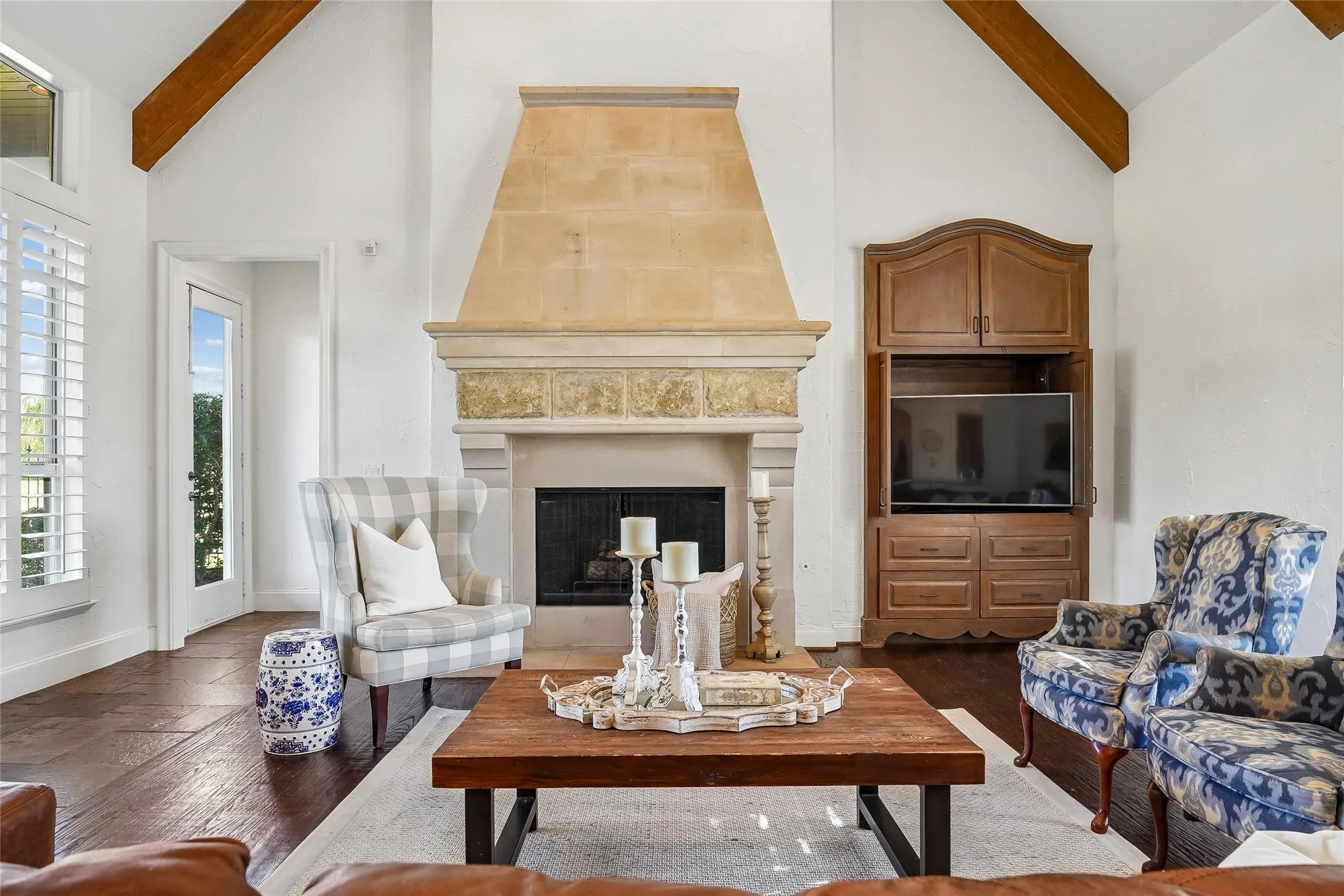 Vaulted ceilings with exposed wood beams, stone fireplace featuring an architectural mantle, dark wood-finish flooring, and built-in cabinetry