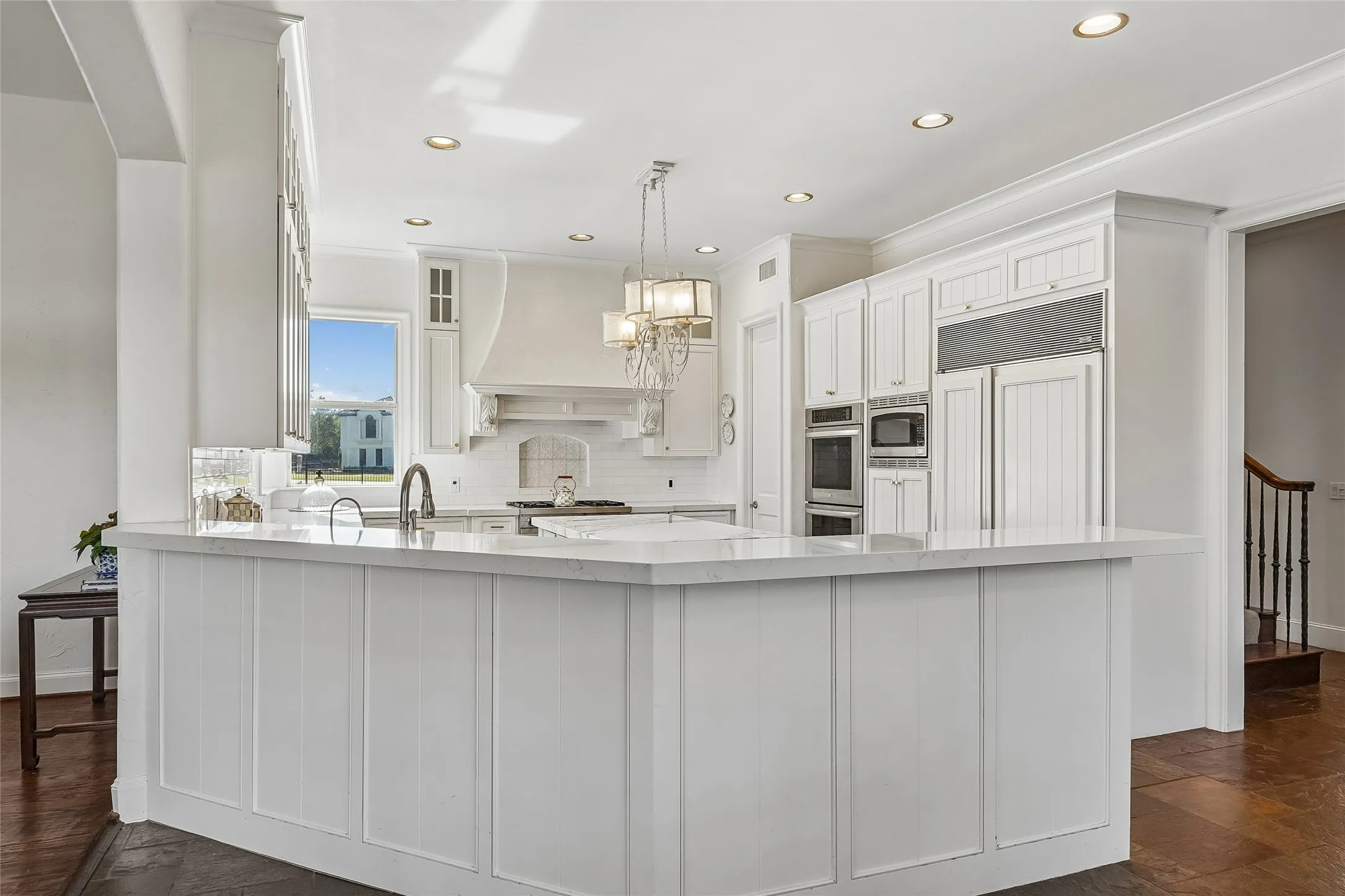 Kitchen featuring a white paneled island with stone countertops, integrated cabinetry, stainless steel double wall ovens, a custom range hood, and recessed lighting
