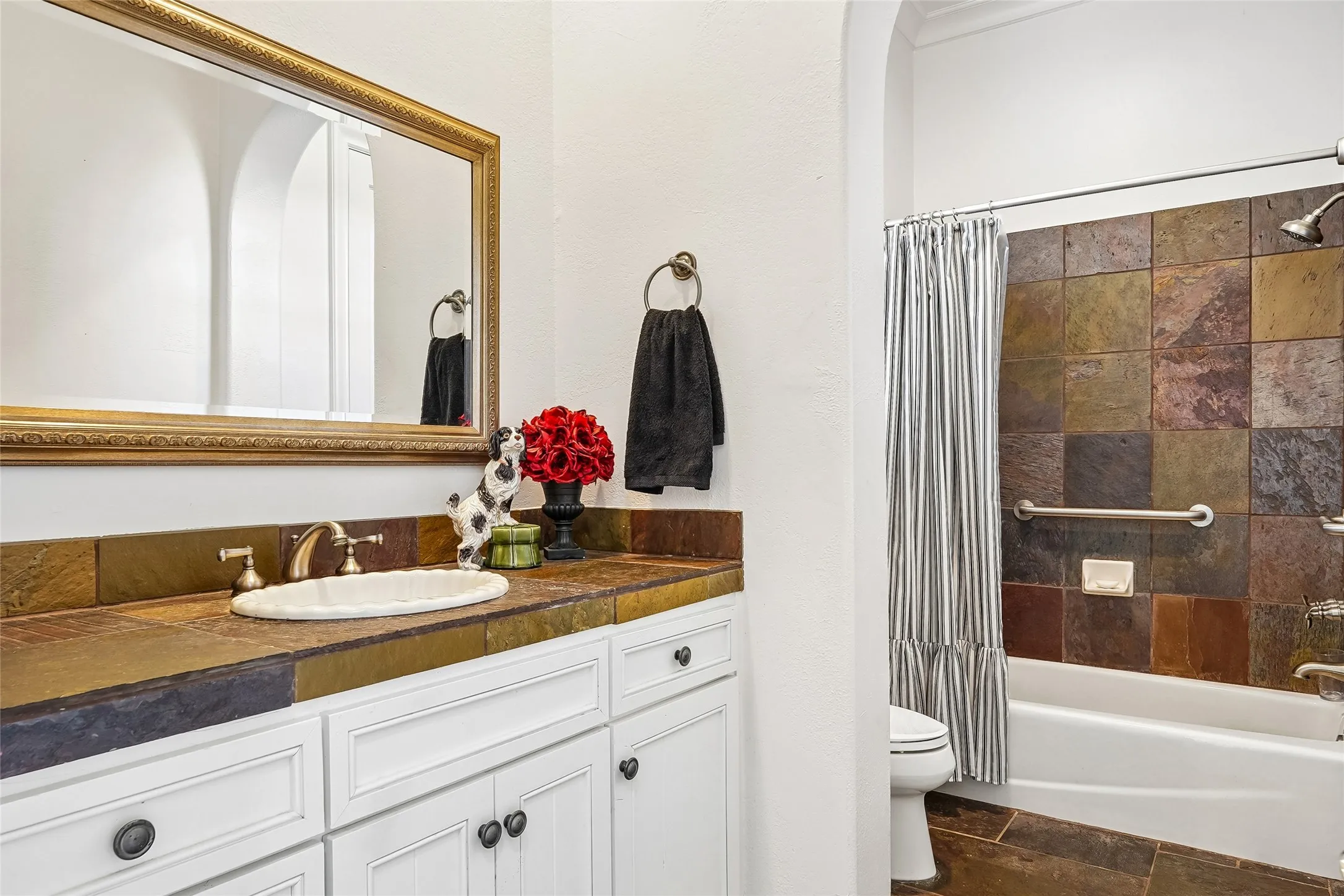 Bathroom featuring white cabinetry, stone tile countertops, an oval drop-in sink, and a tub-shower combination enclosed with multi-tonal stone tile surround