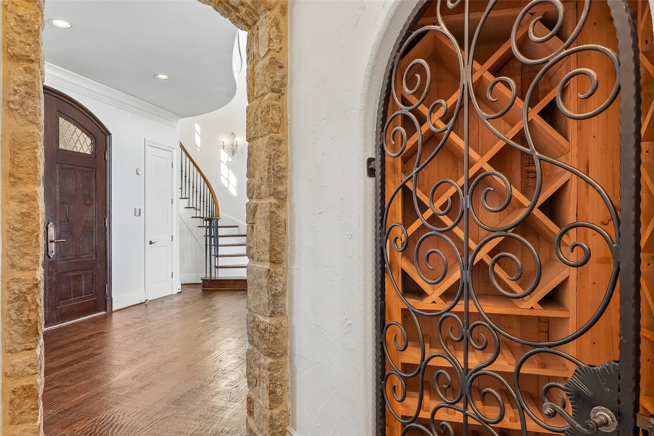Custom wine storage featuring built-in lattice shelving behind an arched iron gate with decorative scrollwork, framed by a textured stone archway