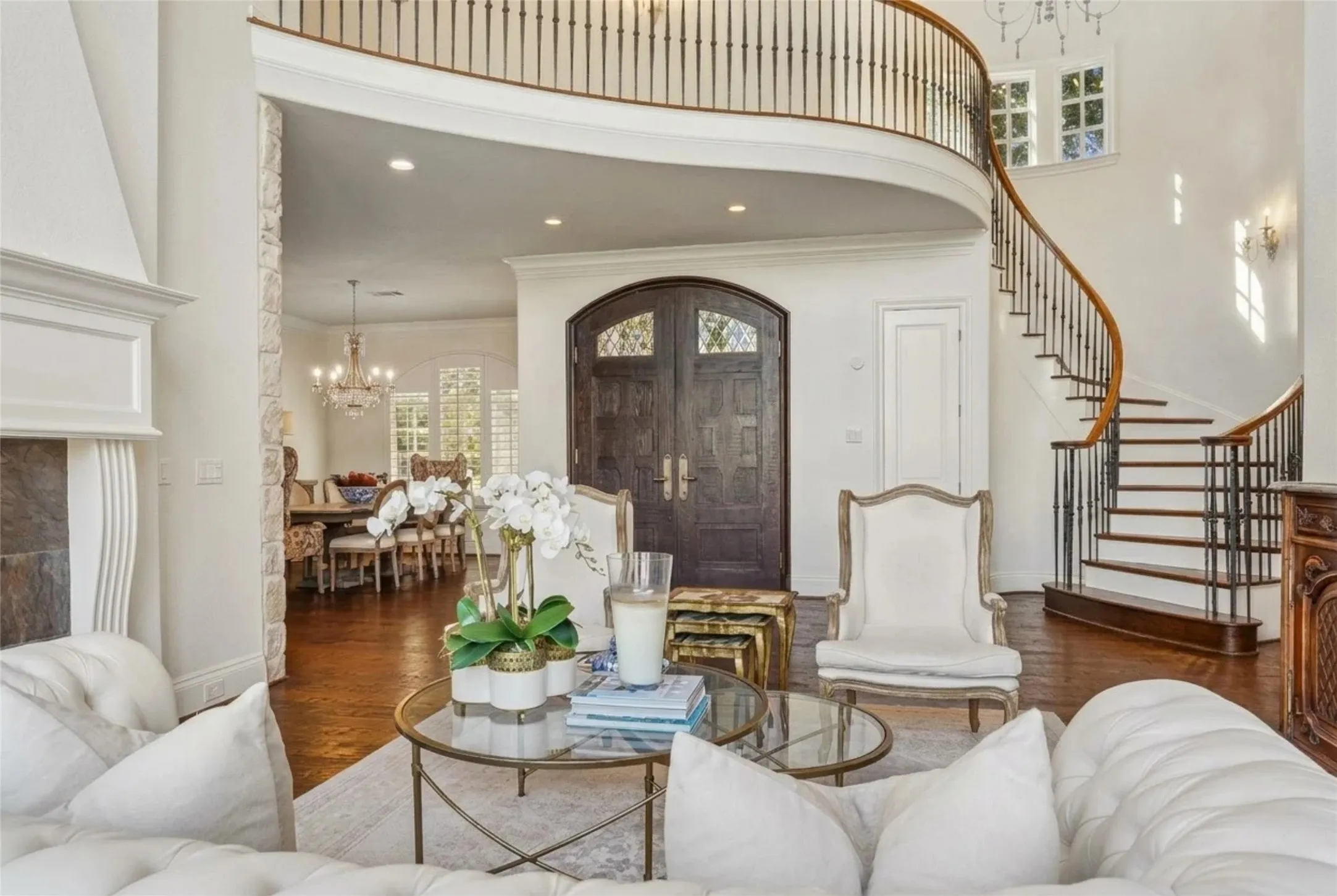 Curved staircase with iron balusters and wood handrail, arched double-entry doors, stone fireplace surround, and wood-finish flooring