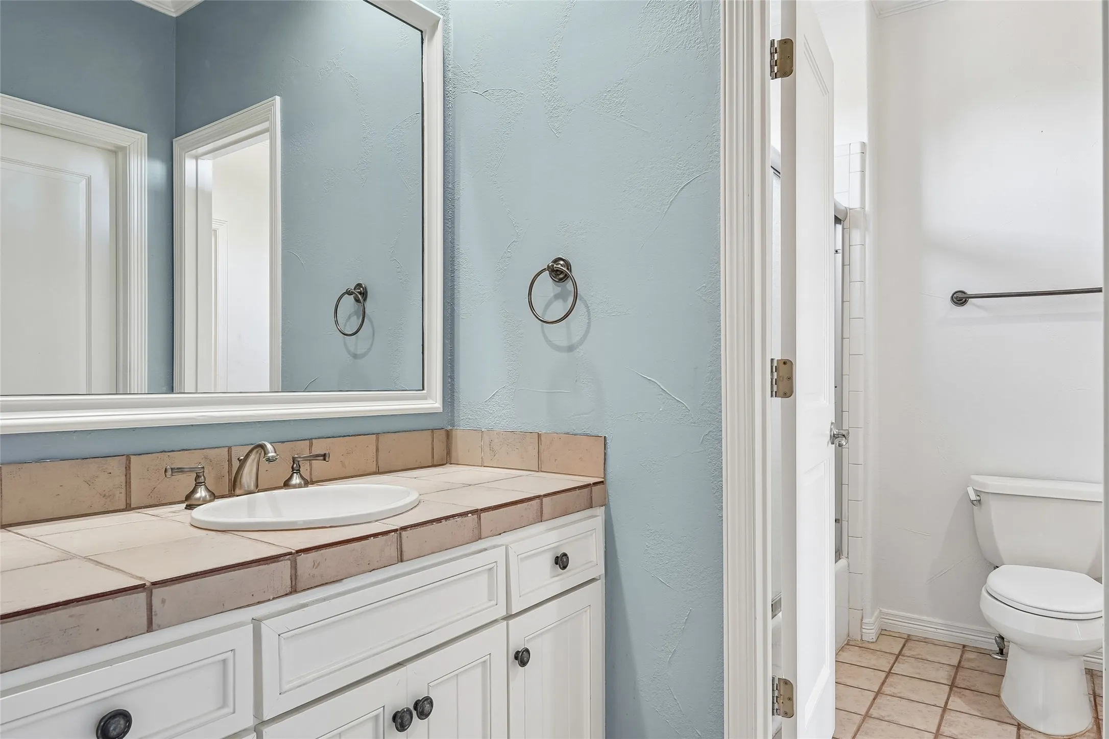 Bathroom featuring white cabinetry, an integrated oval sink, ceramic tile countertops, a framed wall mirror, and tiled flooring