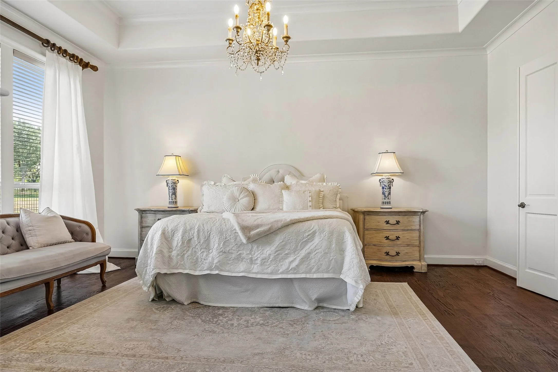 Tray ceiling with crown molding, crystal chandelier, and dark wood-finish flooring