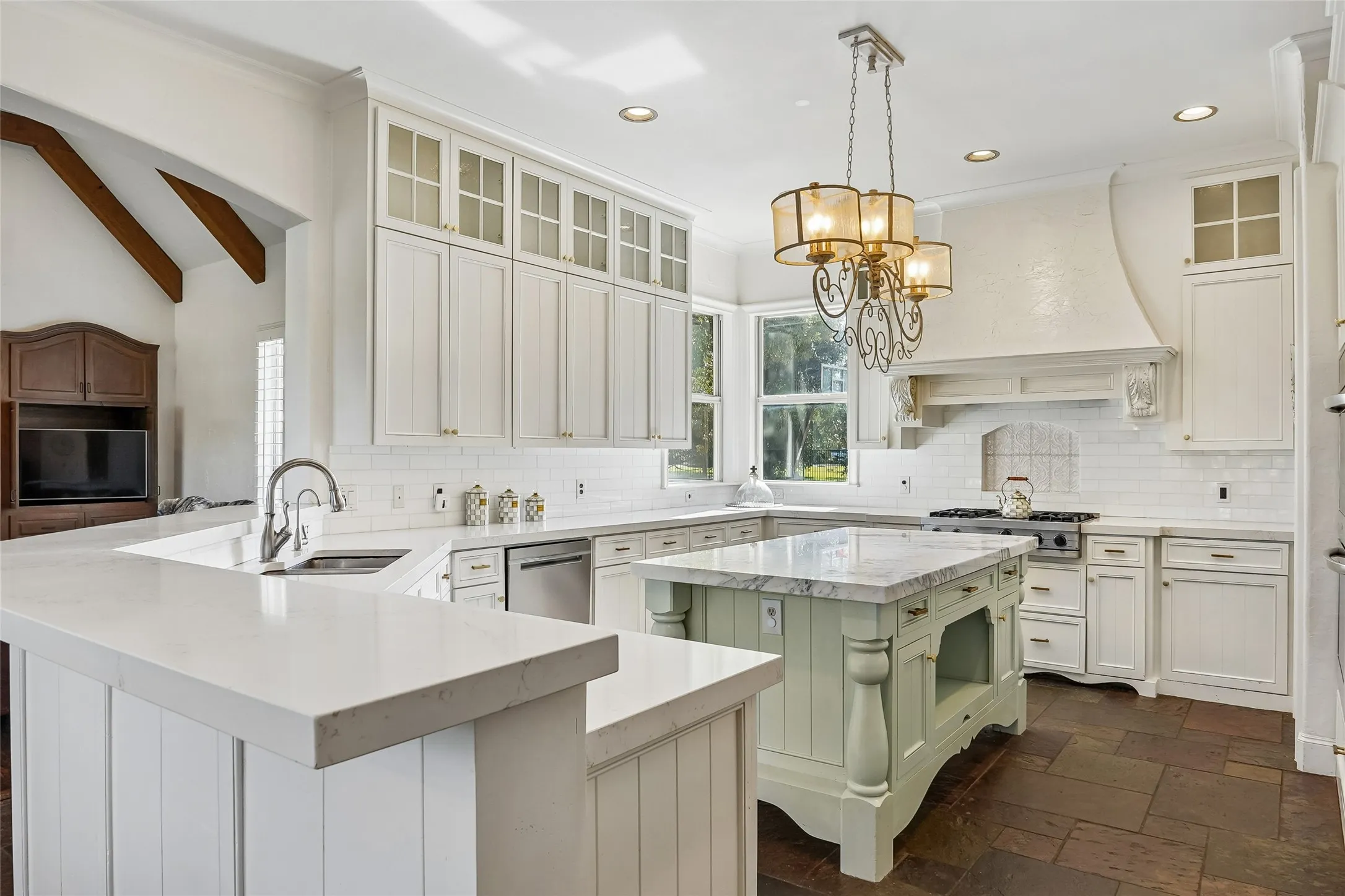 Kitchen featuring white cabinetry with glass-front uppers, a central island with a stone countertop, a custom range hood, recessed lighting, and stone flooring