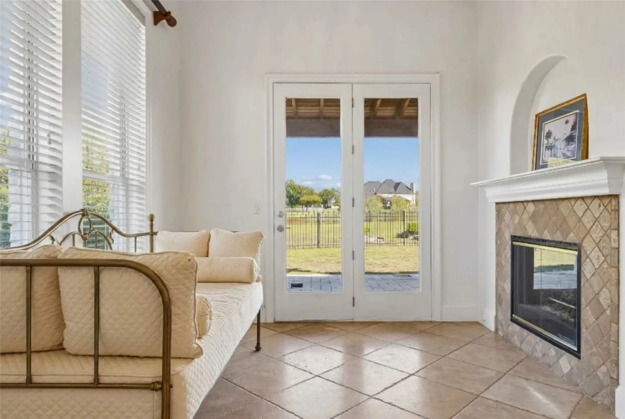 Ceramic tile flooring, fireplace with diamond-patterned stone surround and mantel, arched display alcove, tall windows with blinds, and glass-paneled double doors