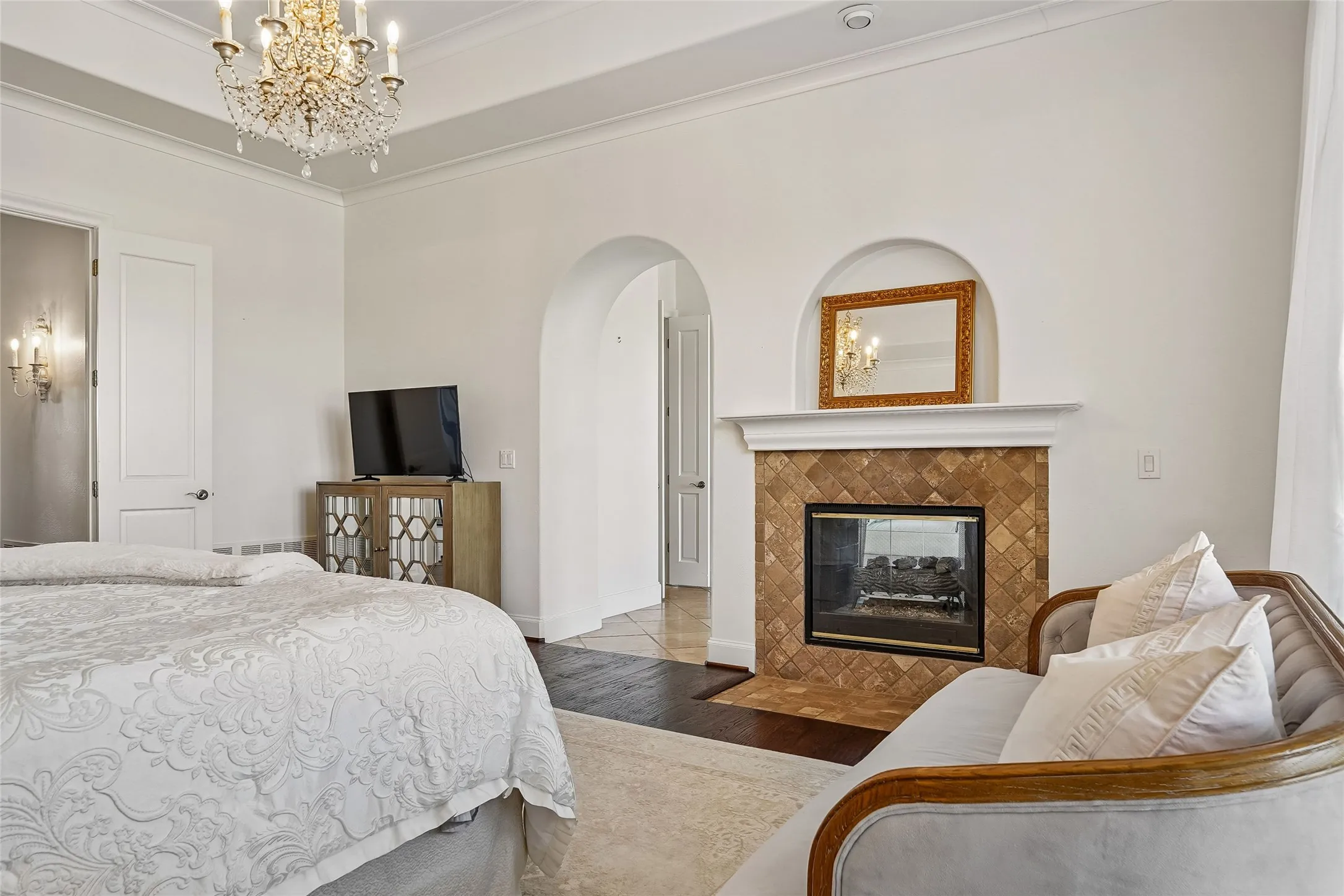 Tray ceiling with an intricate crystal chandelier, arched entryway, and fireplace with decorative tile surround and mantel
