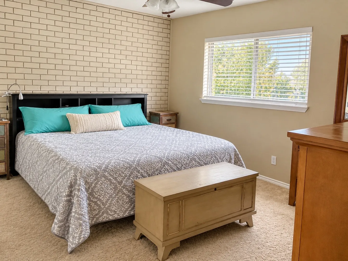 Textured brick accent wall, neutral carpeting, and a double-pane window with installed blinds