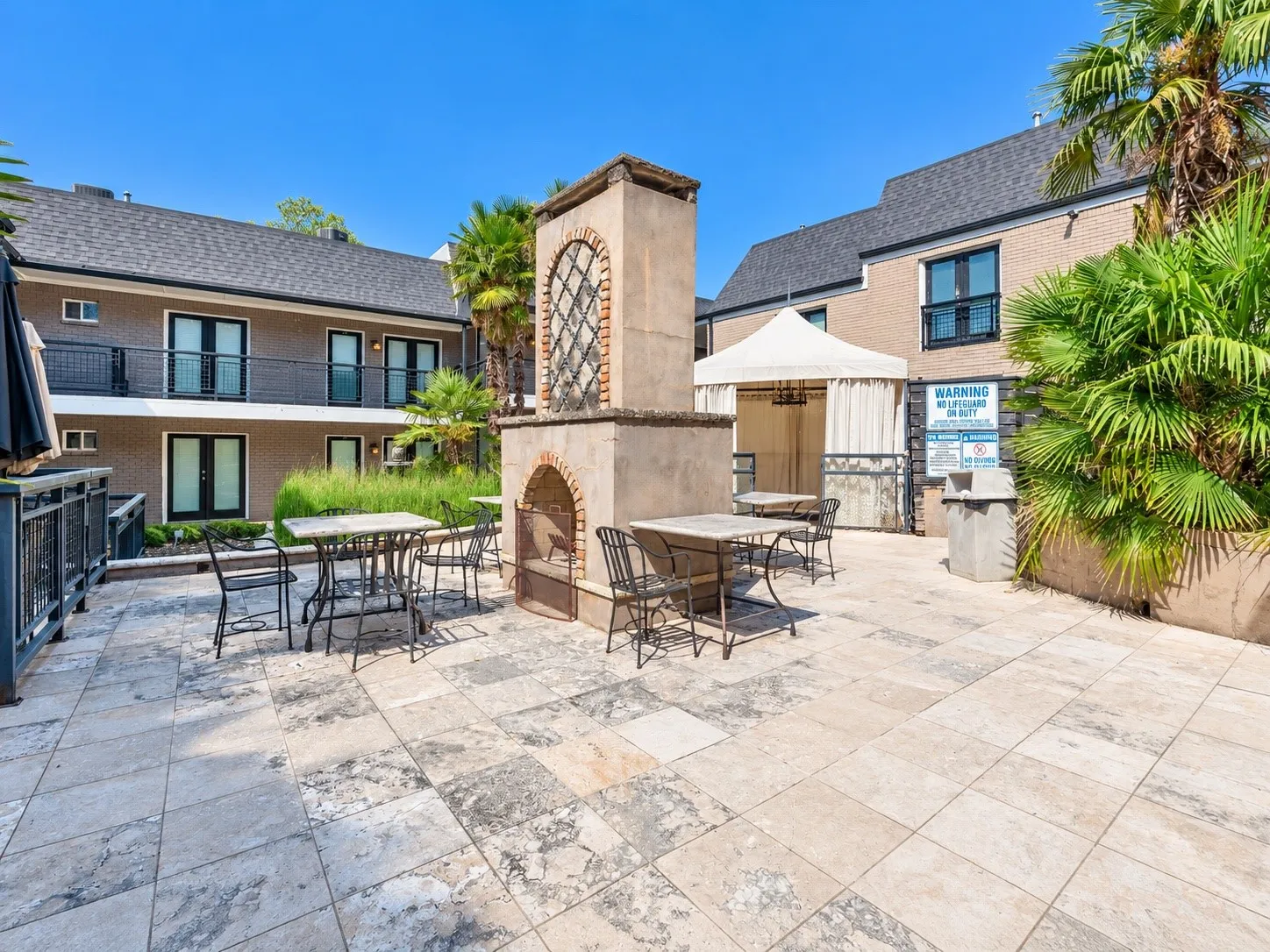 Outdoor patio featuring a stone-clad central fireplace, tile flooring, and integrated wrought-iron railings