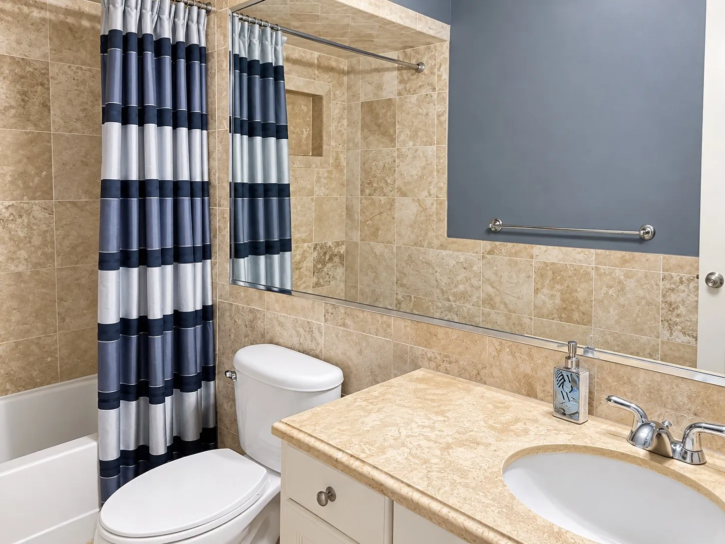 Bathroom featuring floor-to-ceiling stone-tiled walls, a built-in recessed wall niche, a large plate glass mirror, and a vanity with a solid surface countertop and integrated oval sink