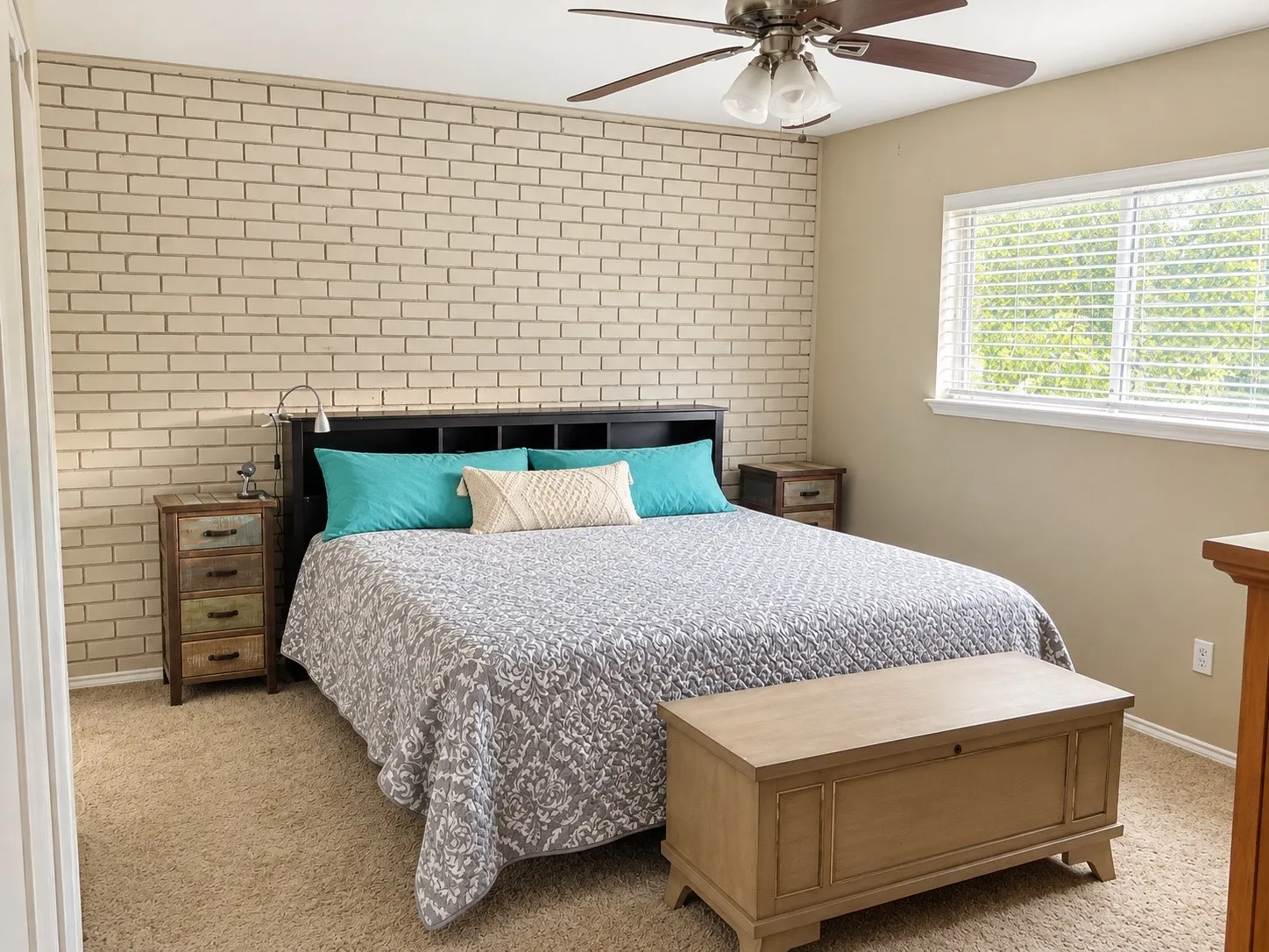 Light-toned brick accent wall, neutral carpeting, and a ceiling fan with integrated lighting
