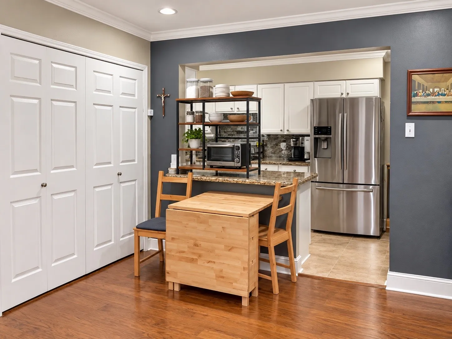 Kitchen featuring white shaker-style cabinetry, stone-finish countertops, stainless steel refrigerator, neutral tile flooring, and wood-finish flooring