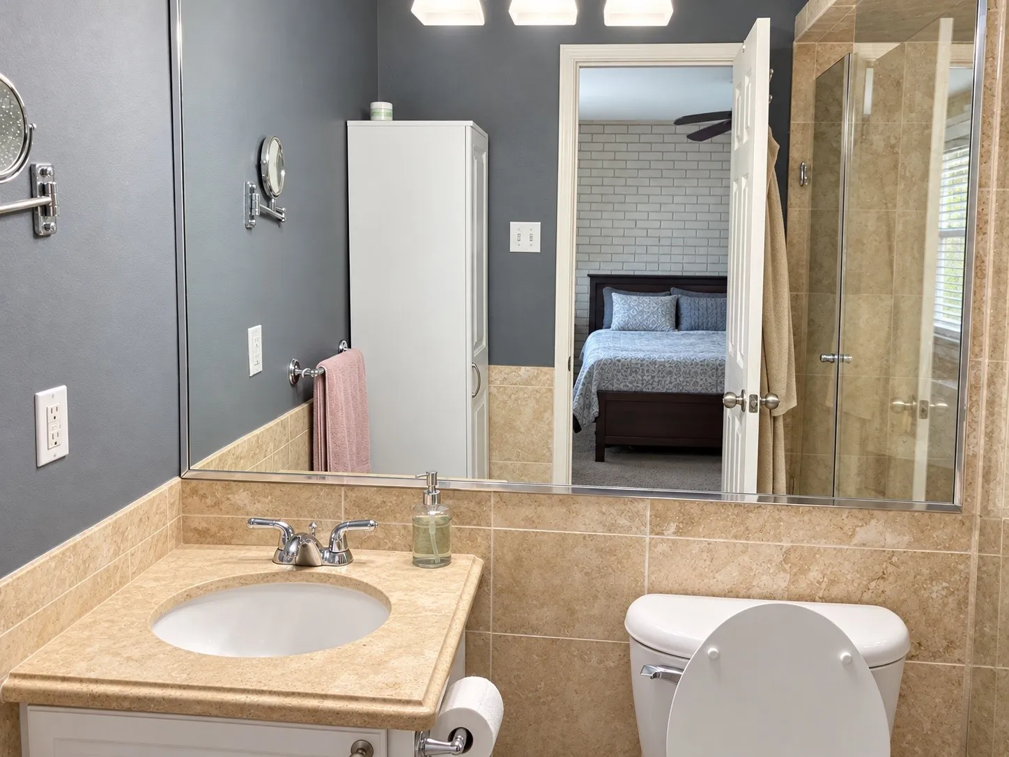 Bathroom featuring a neutral stone-finish countertop, undermount sink, glass-enclosed shower, built-in storage cabinet, and large-scale vanity mirror