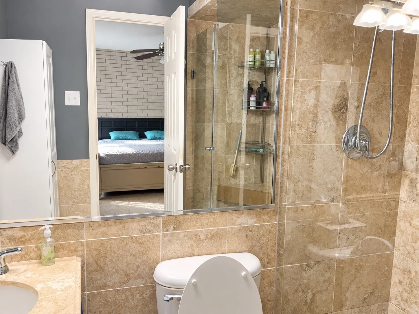 Walk-in shower with stone-tile surround, glass enclosure, and multi-setting showerhead, paired with a matching stone-tile backsplash and vanity countertop