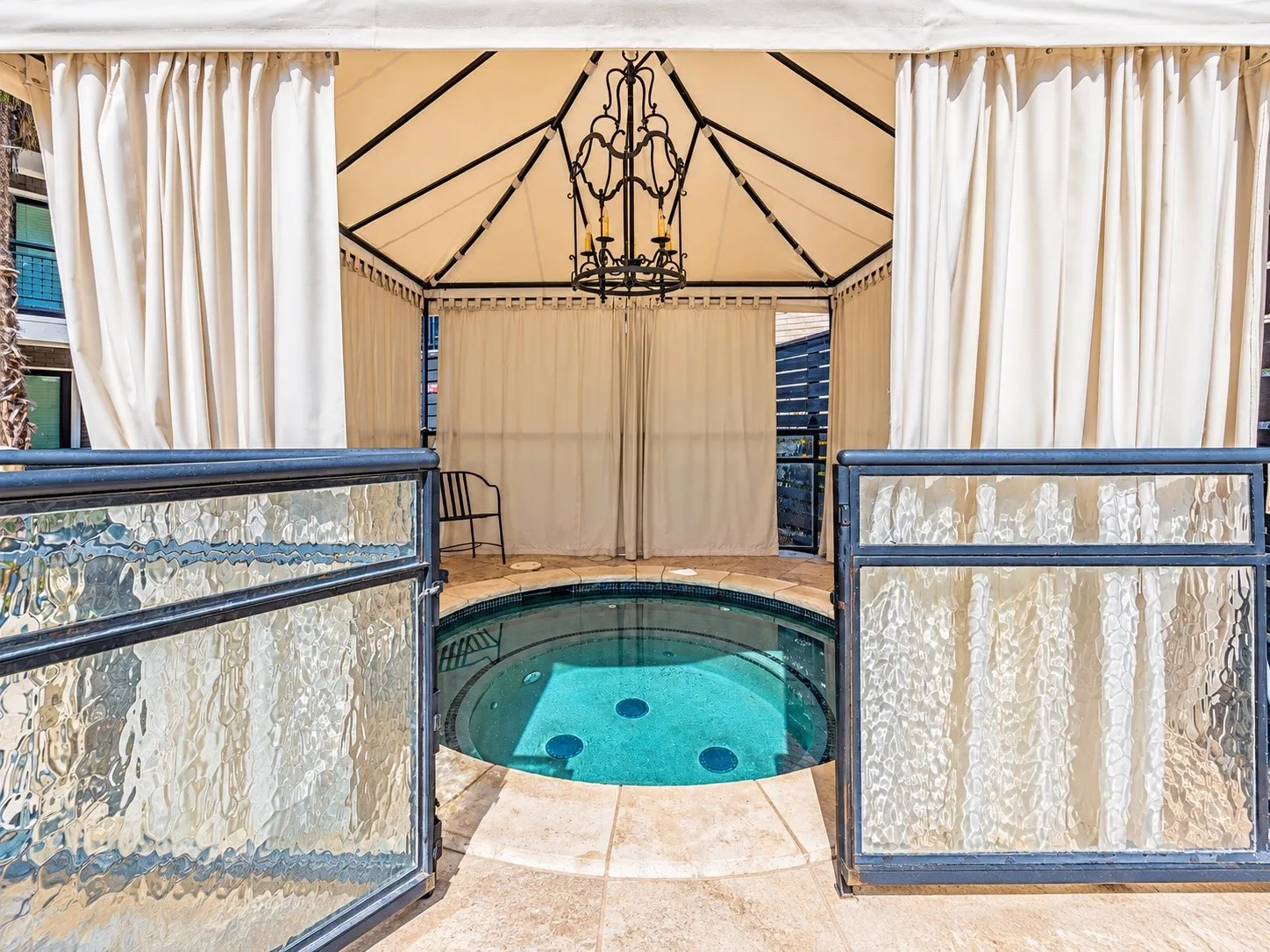 Outdoor spa featuring a circular in-ground basin, stone-tile surround, metal-frame gazebo, and wrought-iron chandelier