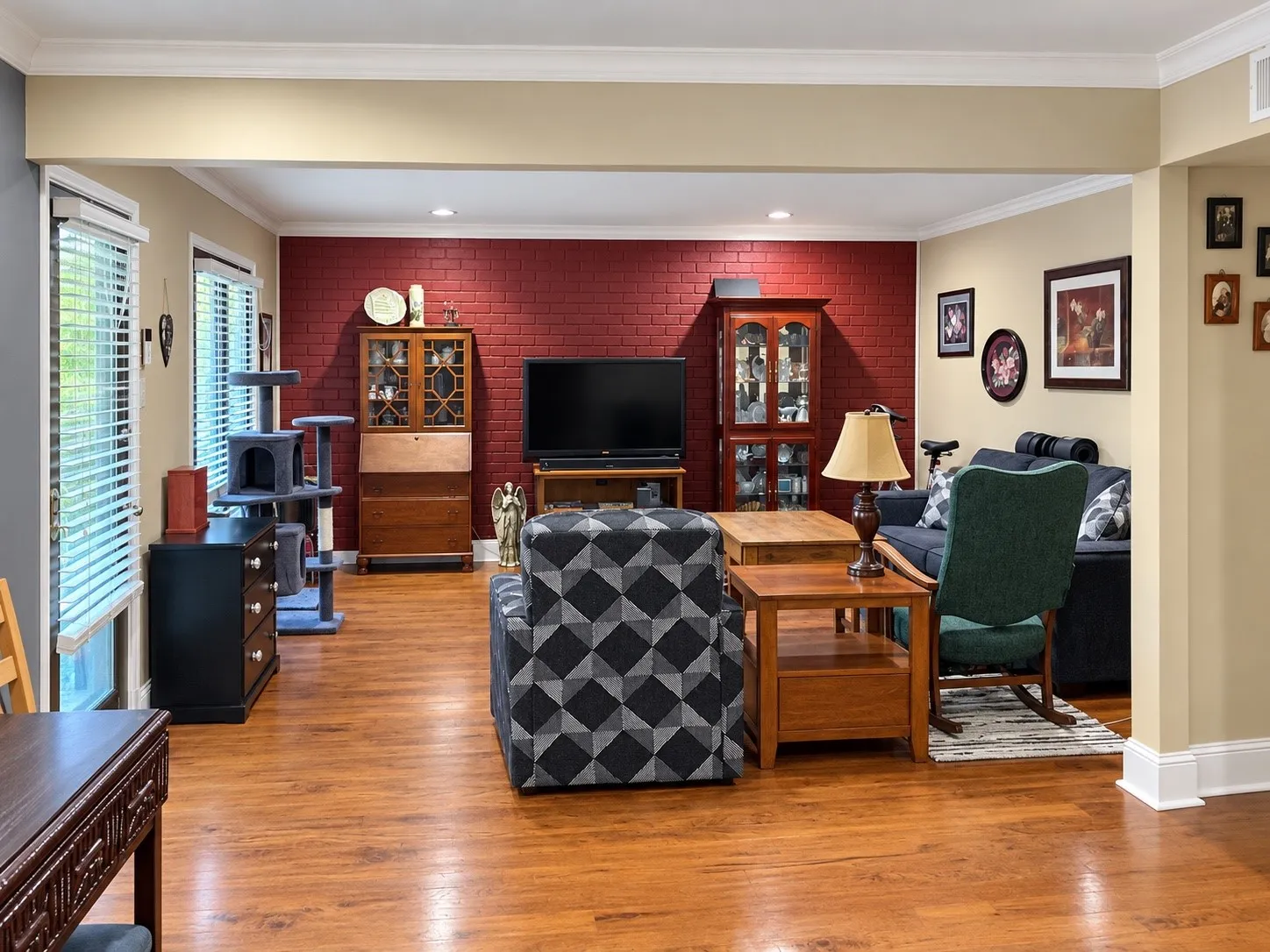 Living area featuring a red painted brick accent wall, wood-finish flooring, recessed lighting, and crown molding