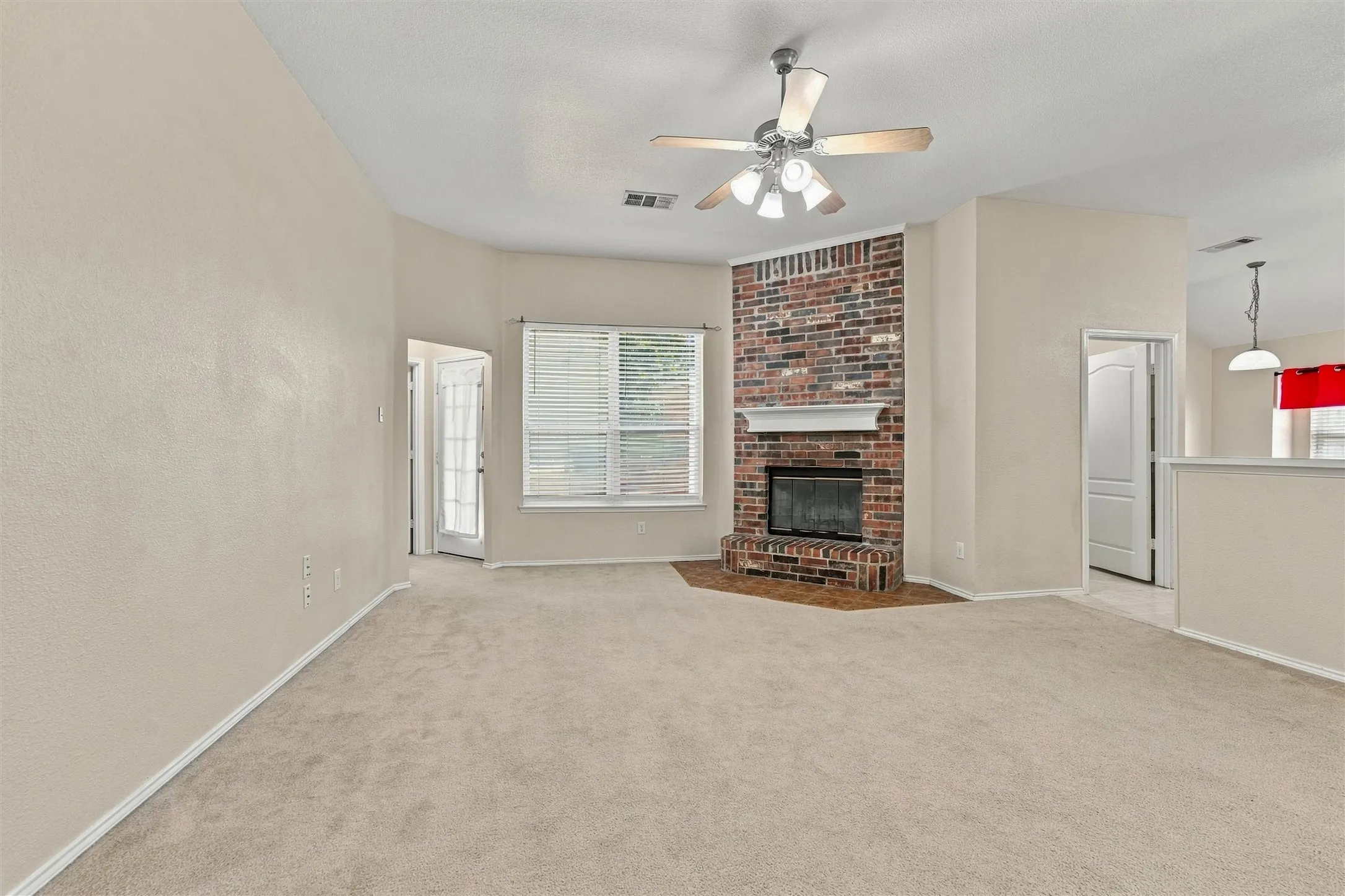 Living area featuring a full-height brick fireplace with a mantle, hearth, carpeted flooring, vaulted ceiling, and a ceiling fan with multi-light fixture
