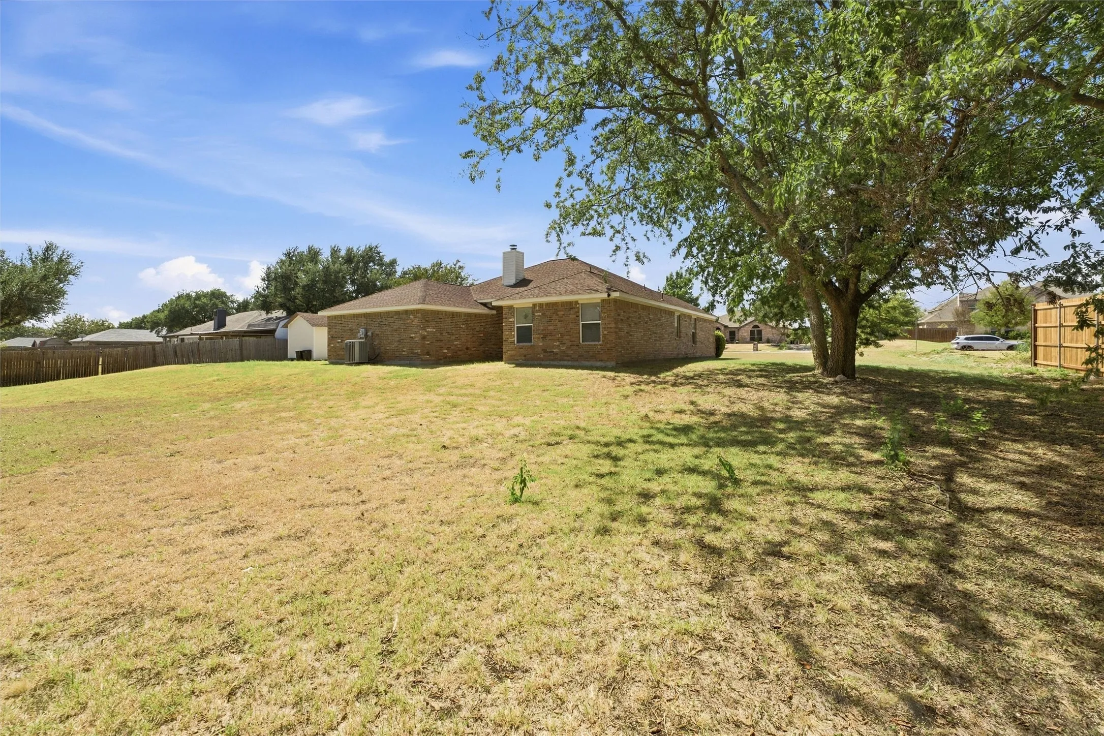 Expansive backyard featuring a brick exterior residence, mature canopy tree, wood privacy fencing, and a chimney stack