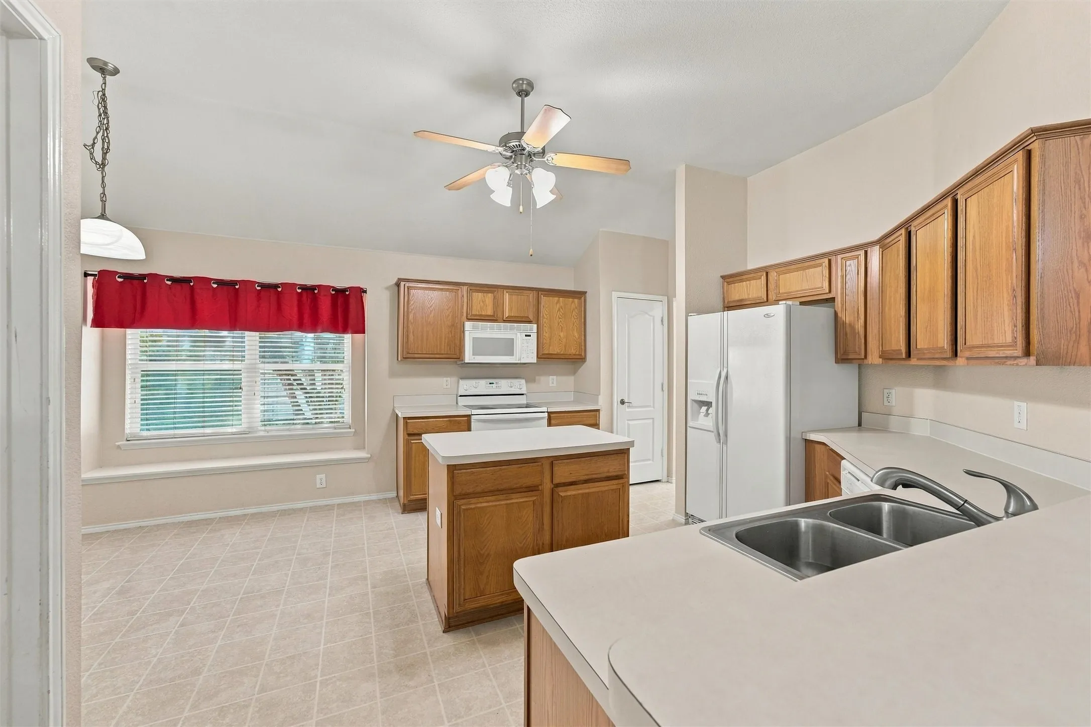 Kitchen featuring wood cabinetry, a central island, neutral countertops, a double-basin stainless steel sink with a goose-neck faucet, and a ceiling-mounted fan