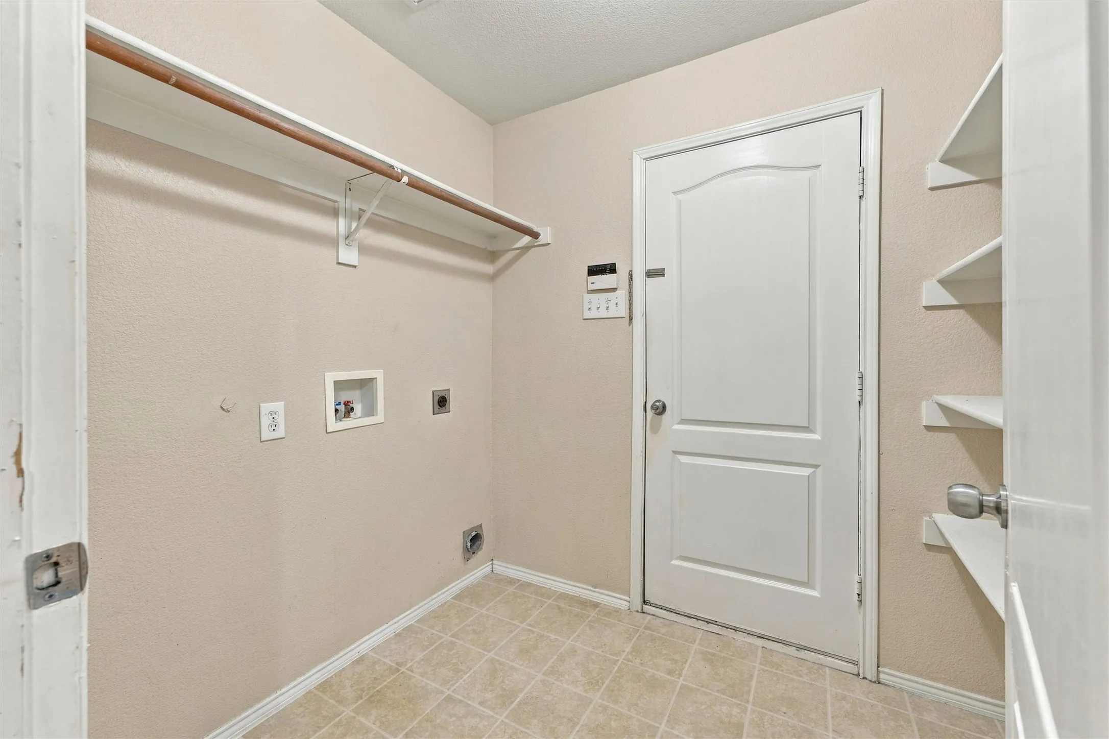 Utility space featuring tiled flooring, built-in open shelving, an overhead rod for hanging storage, and dedicated hookups for laundry appliances