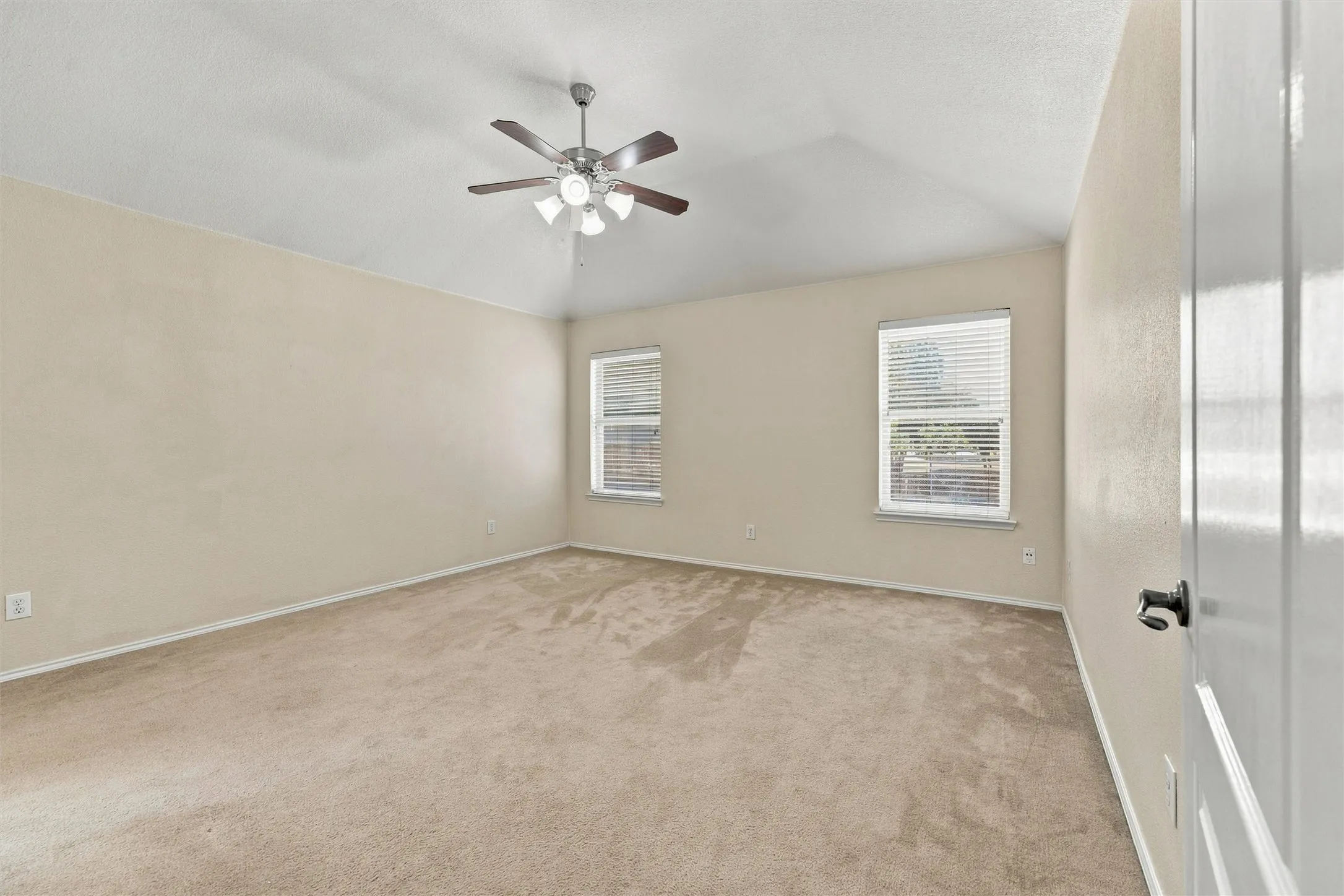 Vaulted ceiling featuring a central multi-blade ceiling fan with integrated light fixture, neutral wall-to-wall carpeting, and two double-pane windows