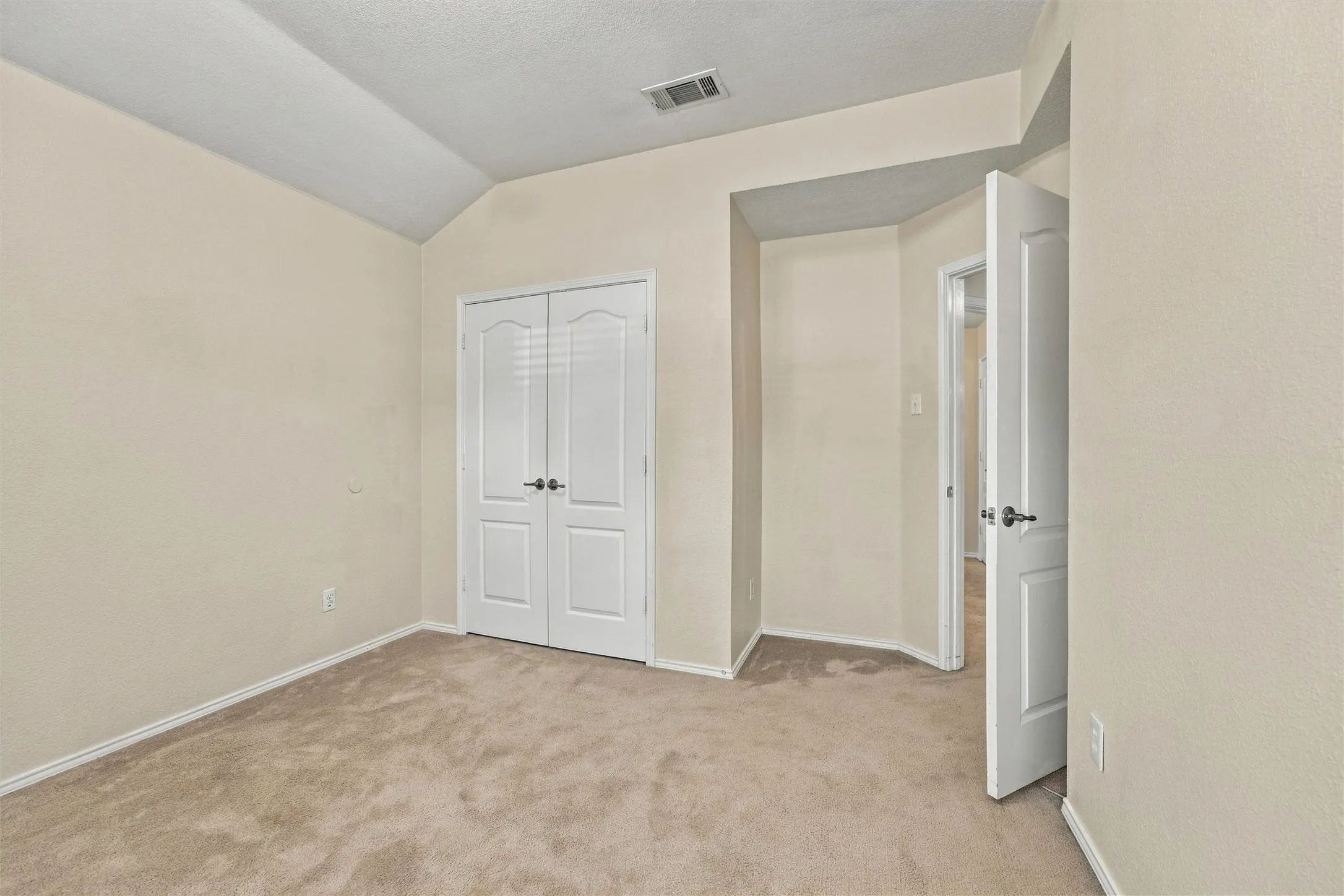 Neutral-toned interior room featuring vaulted ceilings, wall-to-wall carpeting, and double-panel closet doors