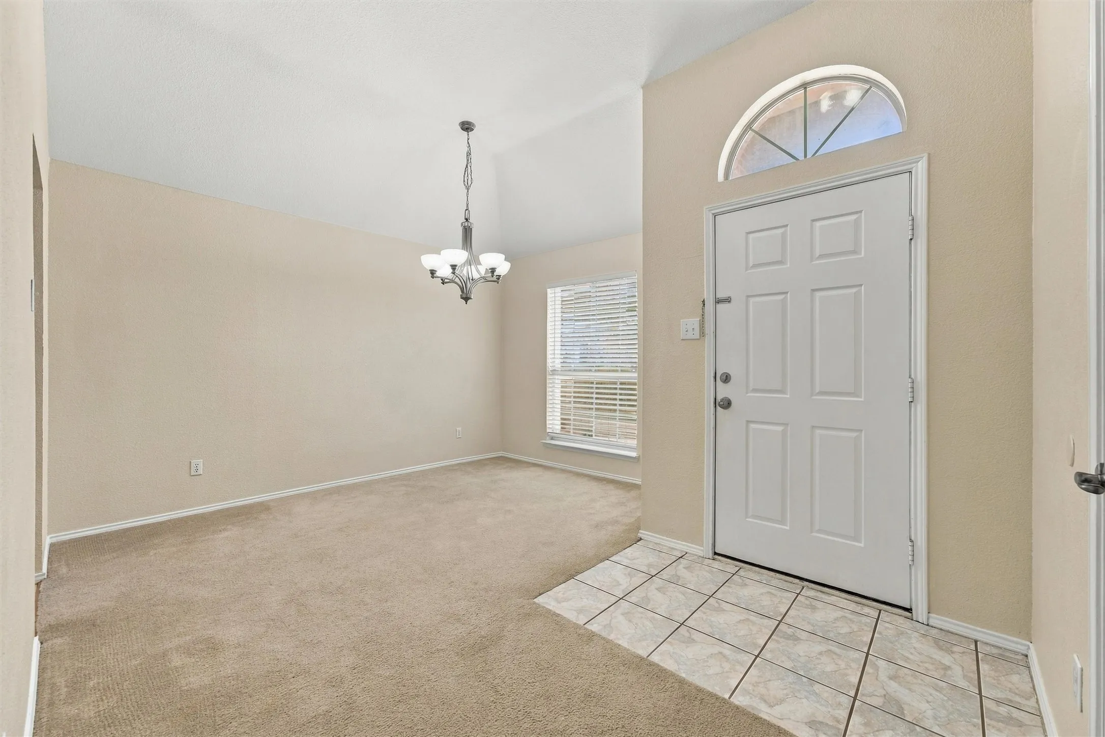 Entryway featuring ceramic tile flooring, vaulted ceilings, a multi-pane front door with an arched transom window, and a hanging multi-light chandelier