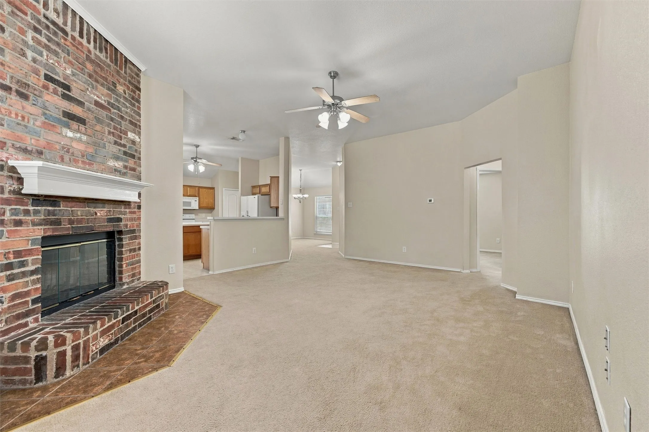Full-height brick fireplace with a prominent mantel and tile hearth, ceiling-mounted light fixtures with paddle fans, and neutral wall-to-wall carpeting