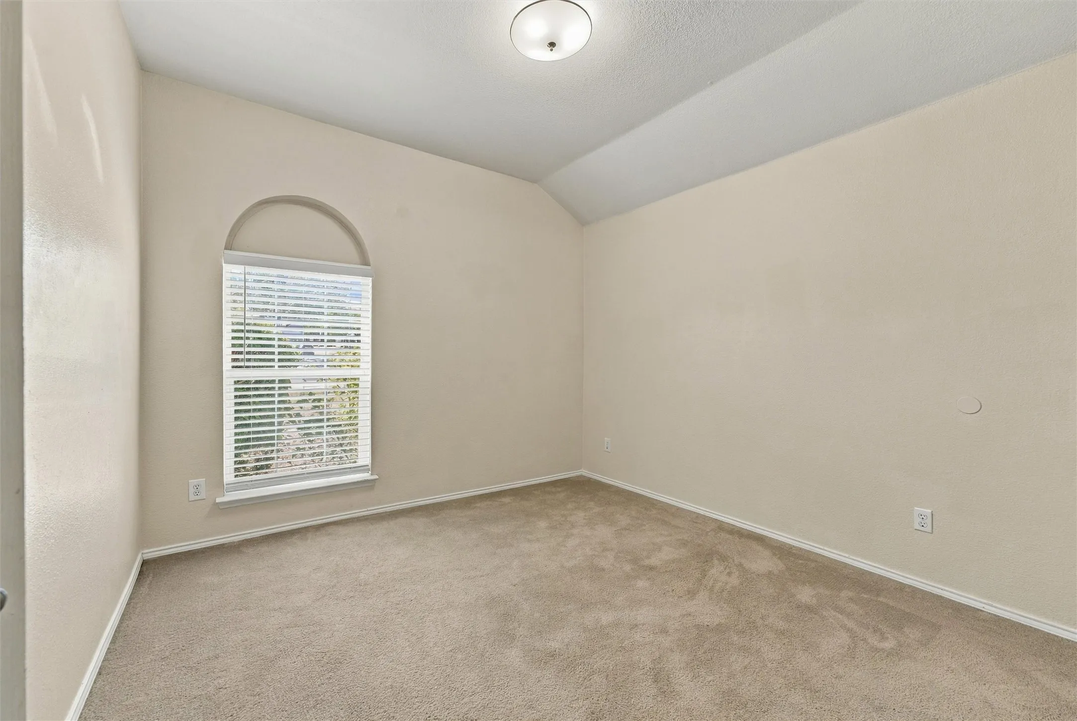 Neutral-toned room featuring a vaulted ceiling, arched window, wall-to-wall carpeting, and a flush-mount ceiling light fixture