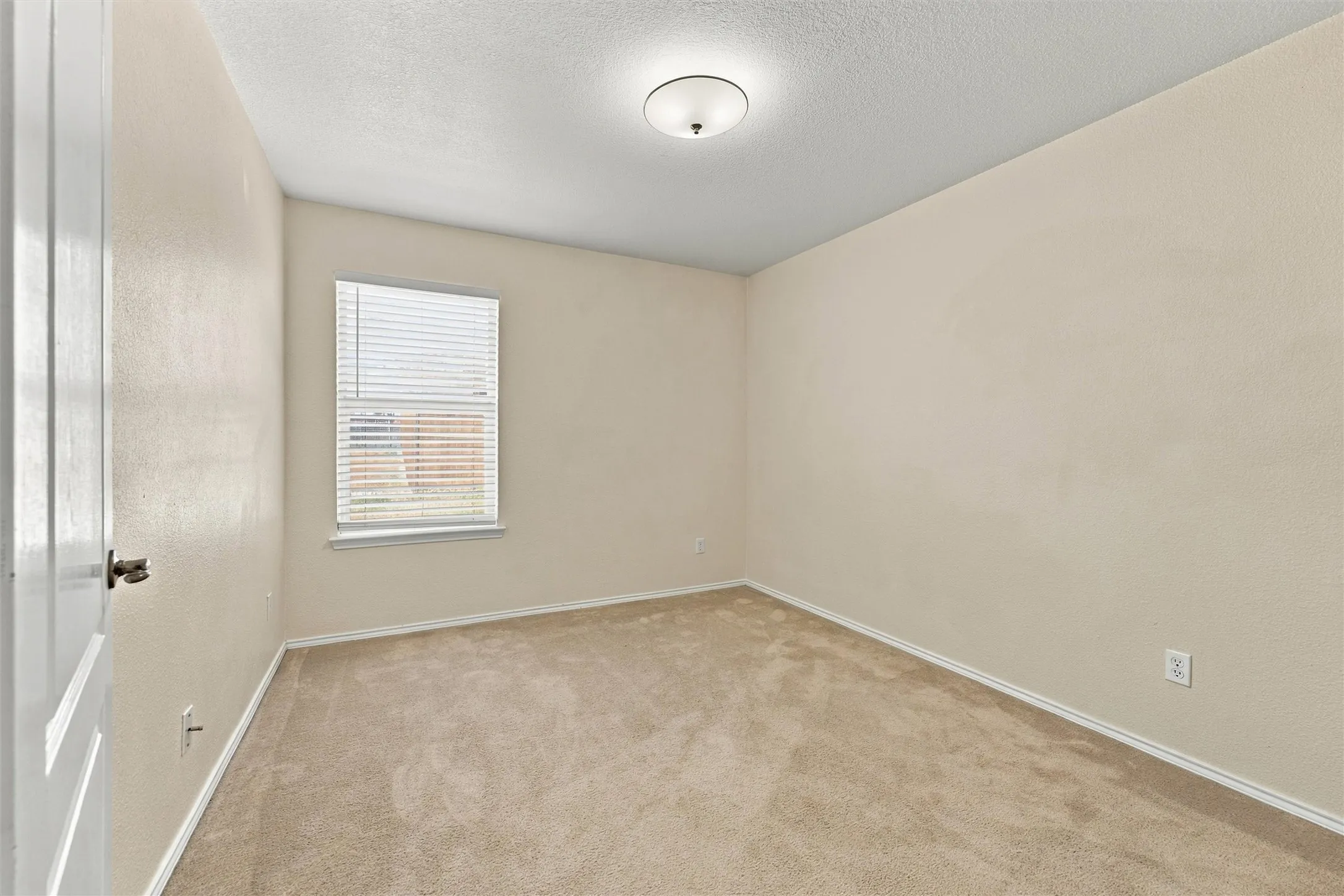 Neutral-toned interior featuring wall-to-wall carpeting, textured wall finish, a single window with horizontal blinds, and a semi-flush mount dome ceiling light