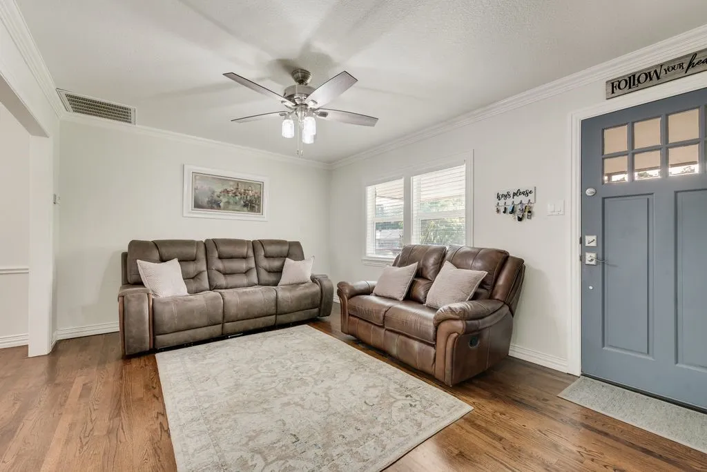 Wood-finish flooring, blue painted front door with multi-pane glass inserts, crown molding, and a multi-blade ceiling fan with integrated lighting