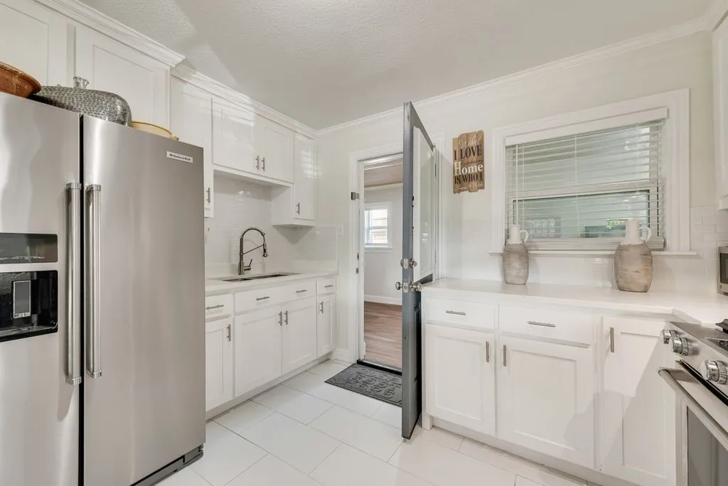 Kitchen featuring white cabinetry, solid-surface countertops, subway tile backsplash, stainless steel appliances, and large-format tile flooring