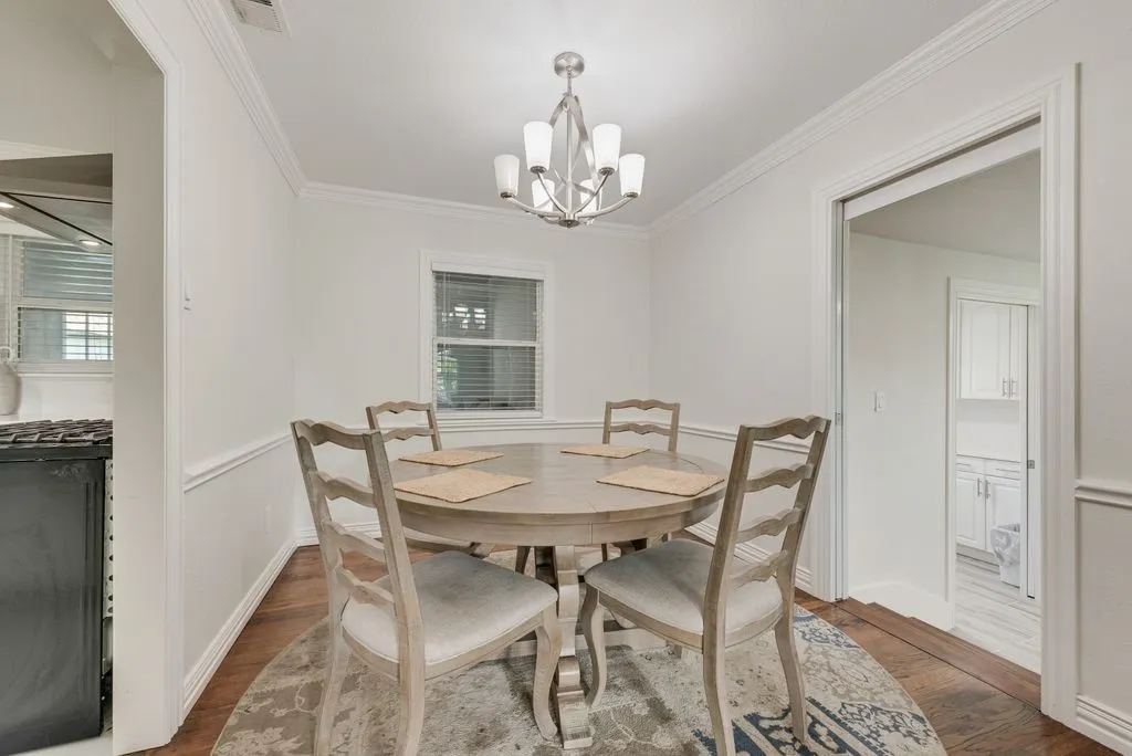 Dining area featuring wood-finish flooring, crown molding, chair rail trim, and a multi-arm chandelier