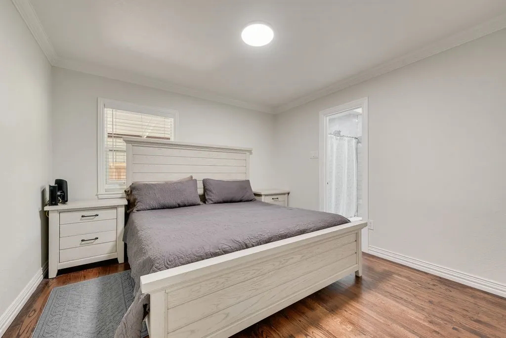 Bedroom featuring wood-finish flooring, crown molding, a flush-mount ceiling light fixture, and a window with white horizontal blinds
