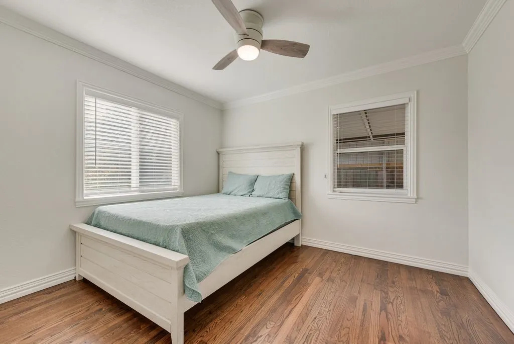 Wood-finish flooring, crown molding, multi-pane windows with horizontal blinds, and a central ceiling fan with integrated lighting