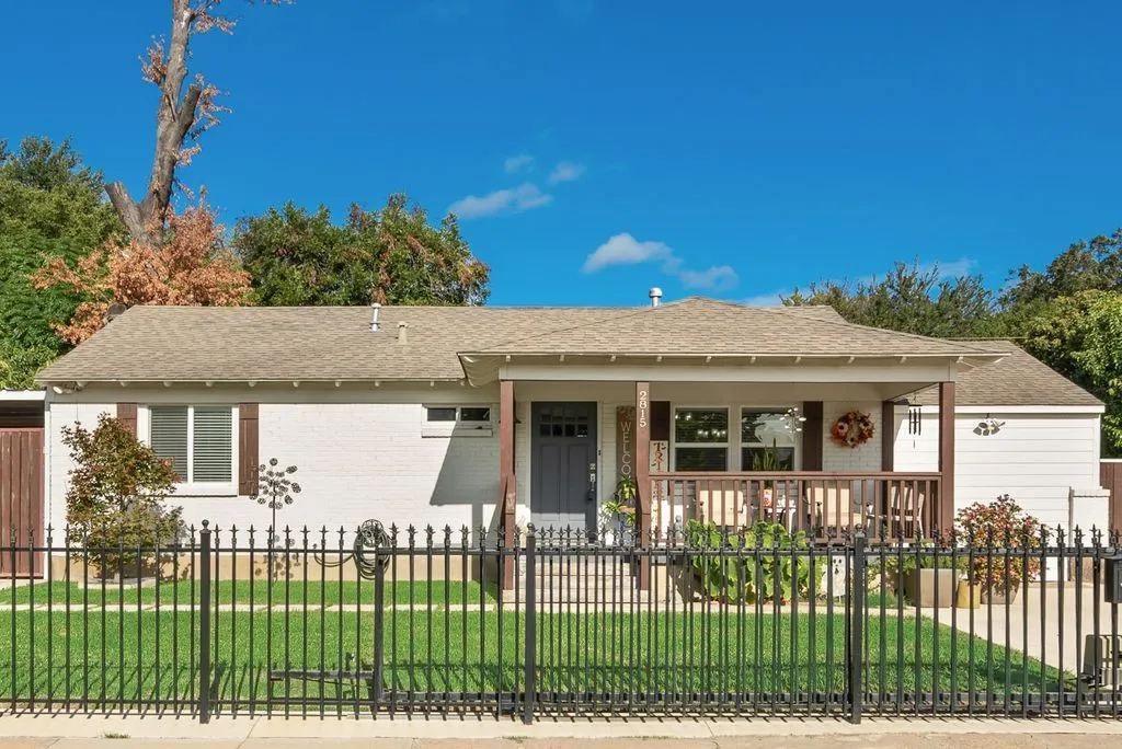 Single-story residence featuring a painted brick exterior, covered front porch with wood-finish posts, and a black metal perimeter fence