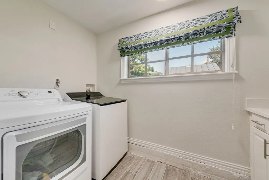 Laundry room featuring neutral wall finishes, tile flooring, a window with a valance, and white cabinetry with a solid-surface countertop