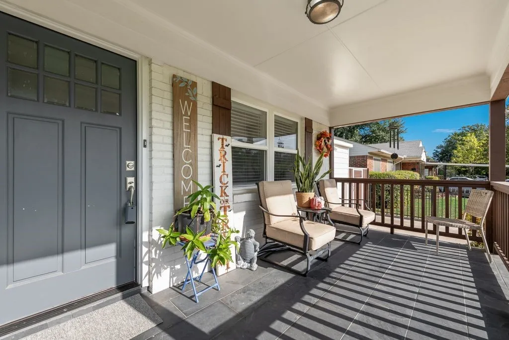 Covered front porch featuring dark tile flooring, a painted brick exterior, a multi-pane glass entry door, and a wooden balustrade