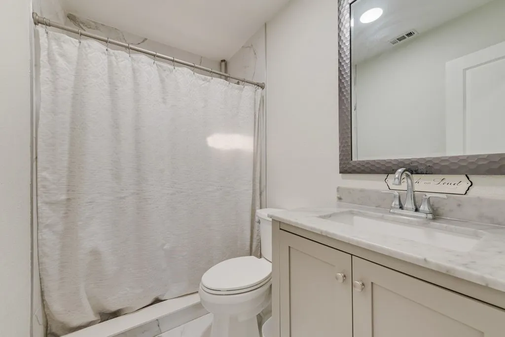 Bathroom featuring a vanity with stone-top basin, undermount sink, brushed-metal faucet, and a large framed mirror