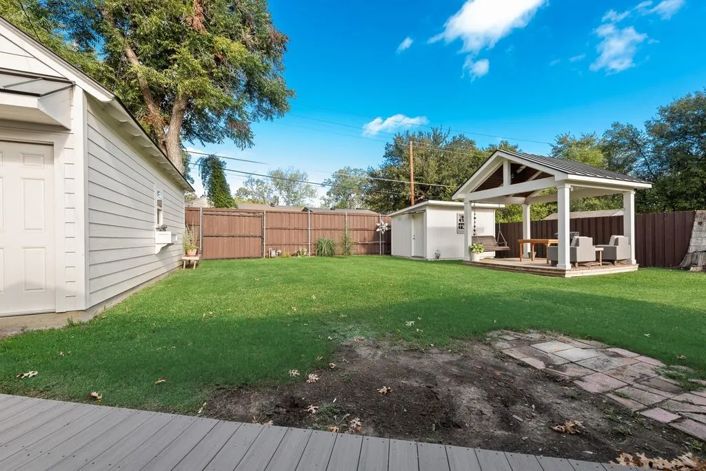 Expansive backyard featuring a manicured lawn, detached storage structure, covered open-air pavilion, and perimeter wood privacy fencing