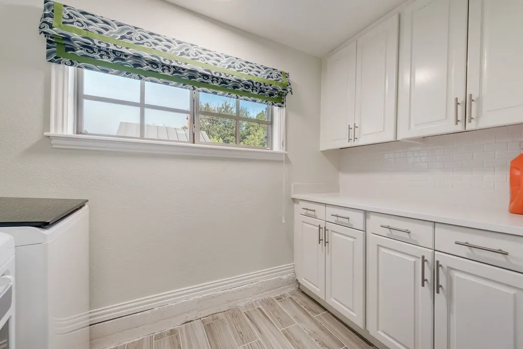 Laundry area featuring white shaker-style cabinetry, solid-surface countertops, white subway tile backsplash, and wood-finish tile flooring
