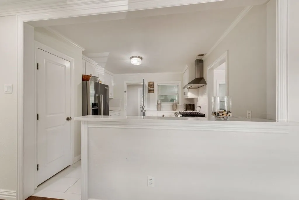 Kitchen featuring white cabinetry, stainless steel appliances, stone-surface breakfast bar, and stainless steel chimney-style range hood